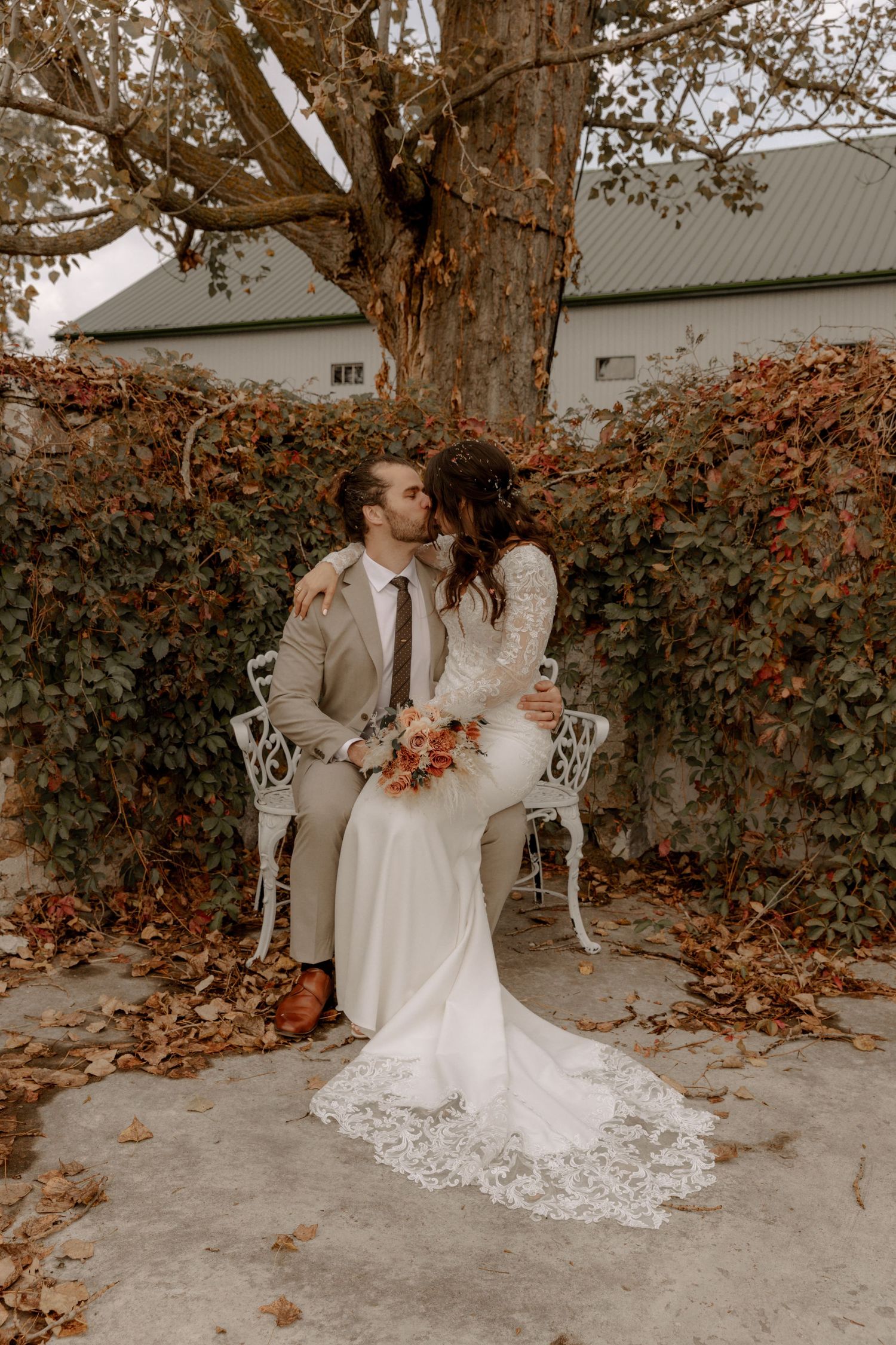 A wedding couple shares an intimate moment on a vintage white chair surrounded by fall foliage and autumn colors.