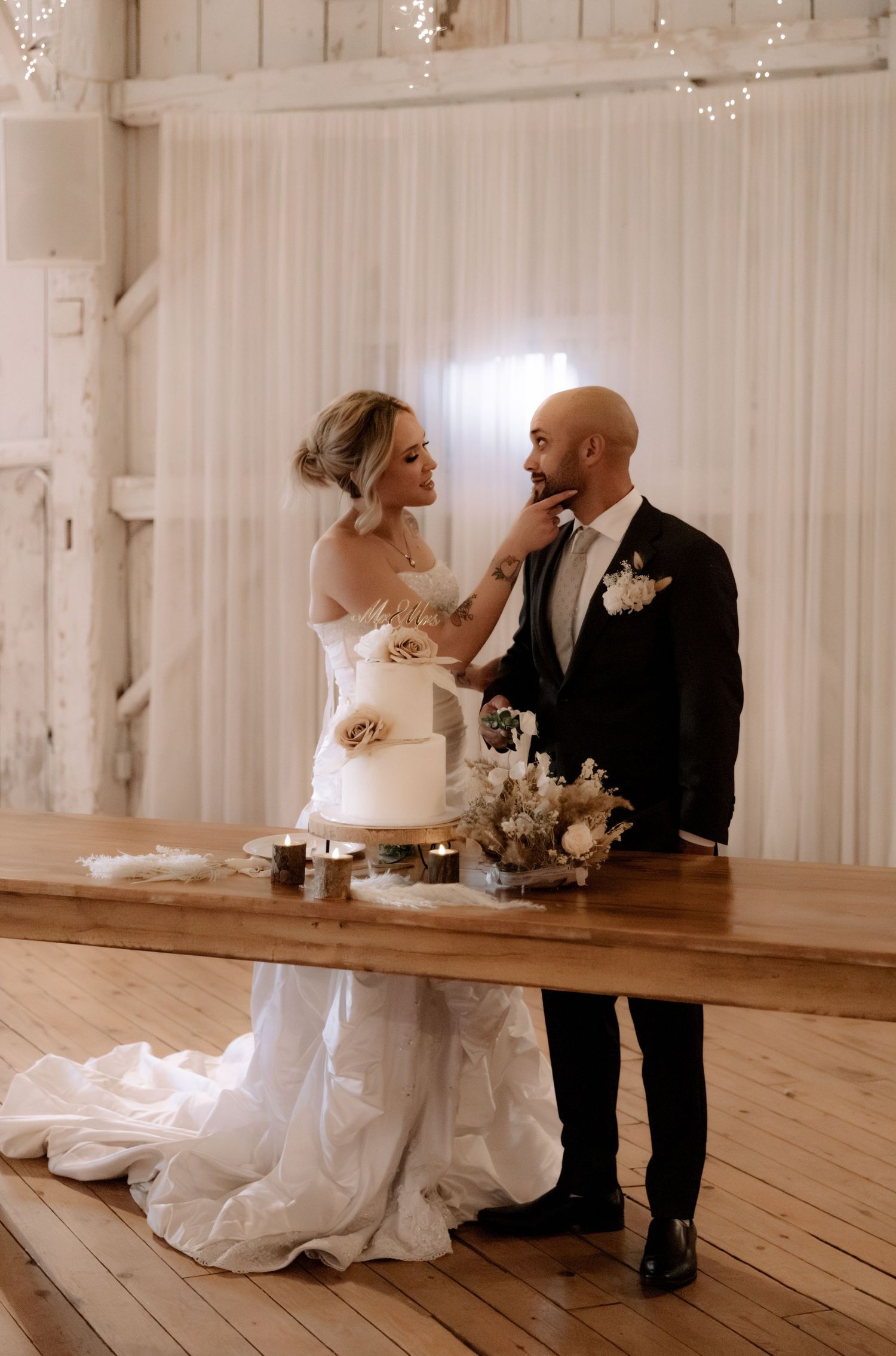 Elegant couple shares an intimate moment during their wedding cake cutting ceremony in a rustic white venue.