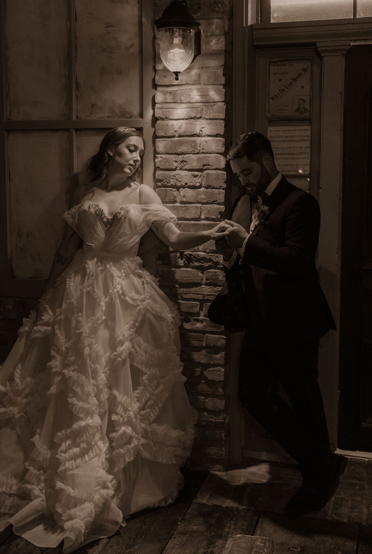 Wedding scene in vintage style showing bride in lace gown and groom by rustic brick doorway.