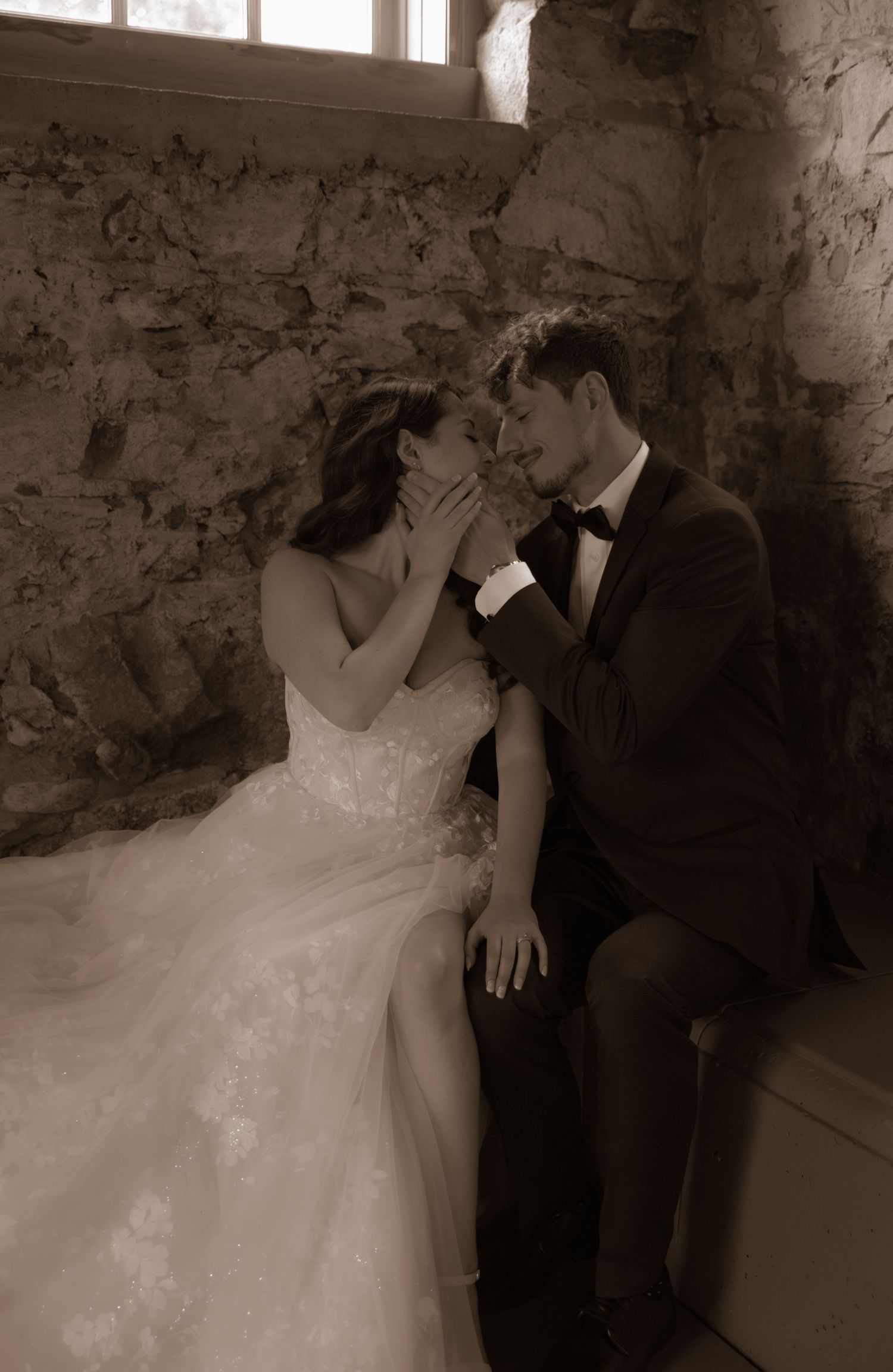 Sepia wedding photo showing tender moment between couple in rustic stone room.