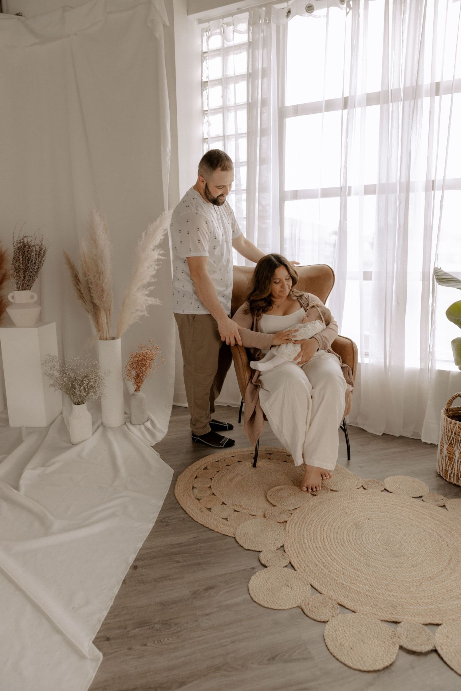 A family shares a tender moment in a bright, minimal room with white decor and a circular jute rug on the floor.