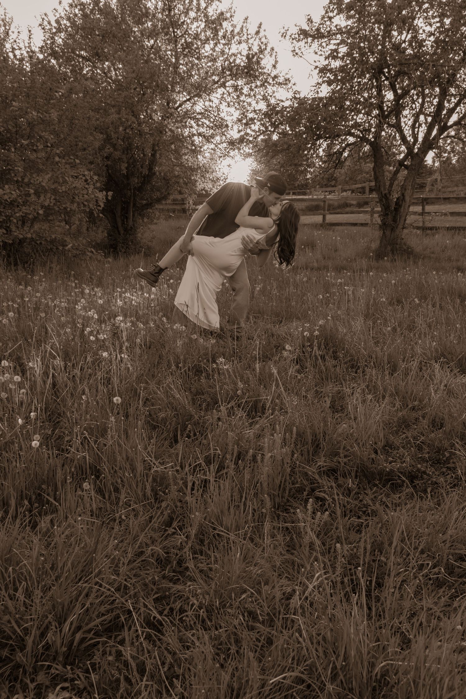 A sepia-toned romantic scene shows a couple dancing in a meadow surrounded by wildflowers and trees.