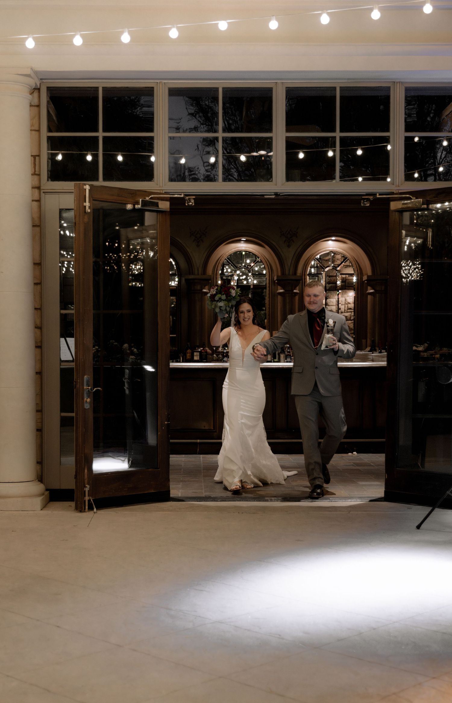 A bride and groom make their grand entrance into an elegantly lit reception venue.