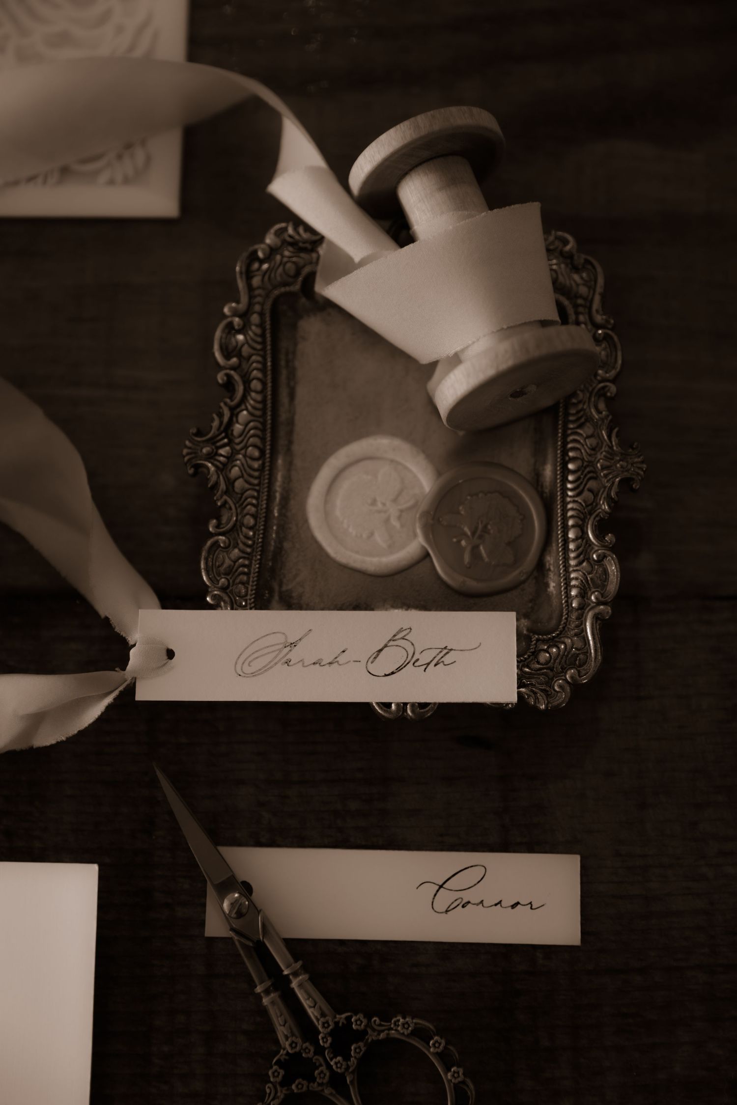 Vintage-style wedding details with wax seal, ribbon and ornate frame on wooden surface.