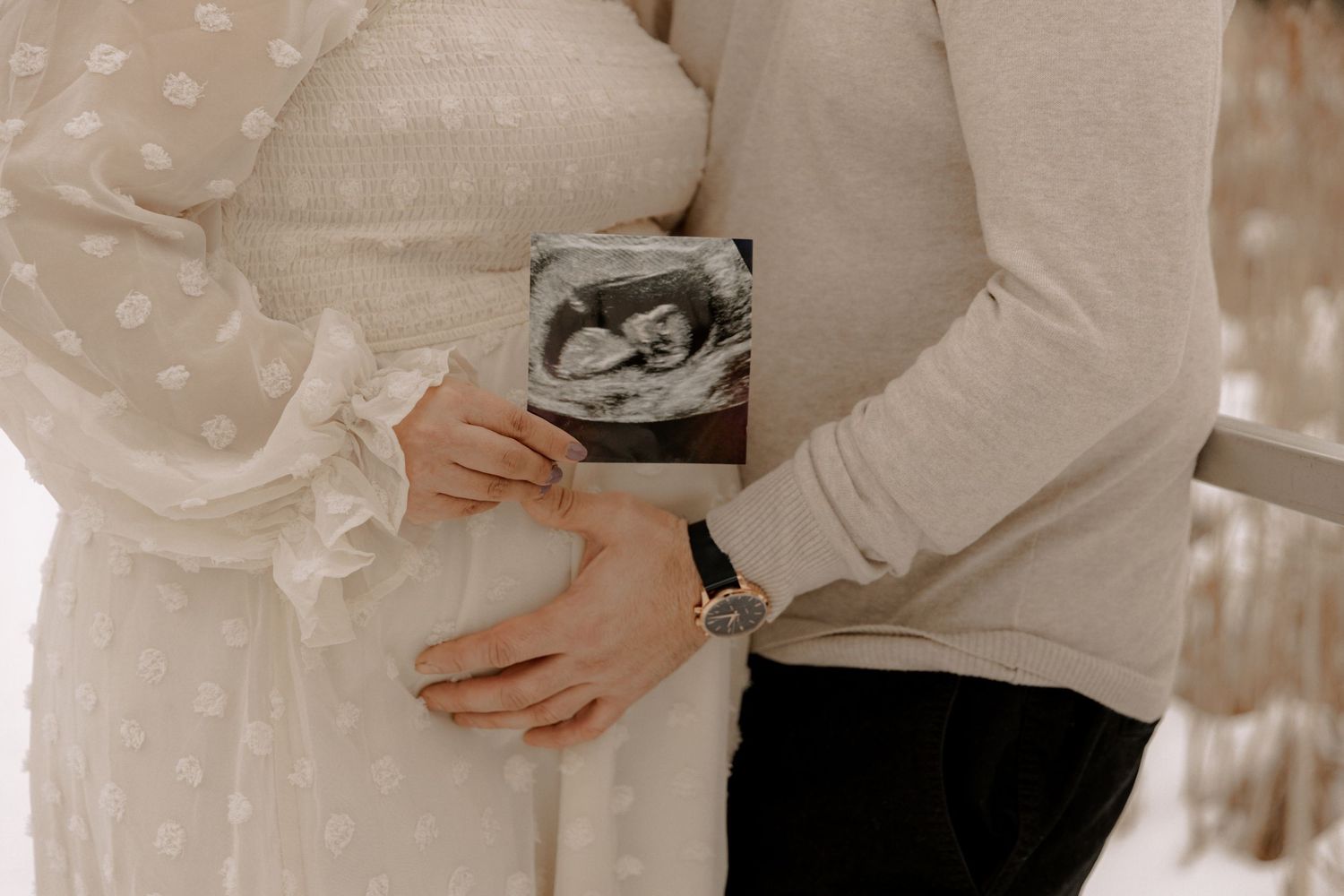 A couple holding a sonogram photo while embracing, sharing a tender pregnancy announcement moment.