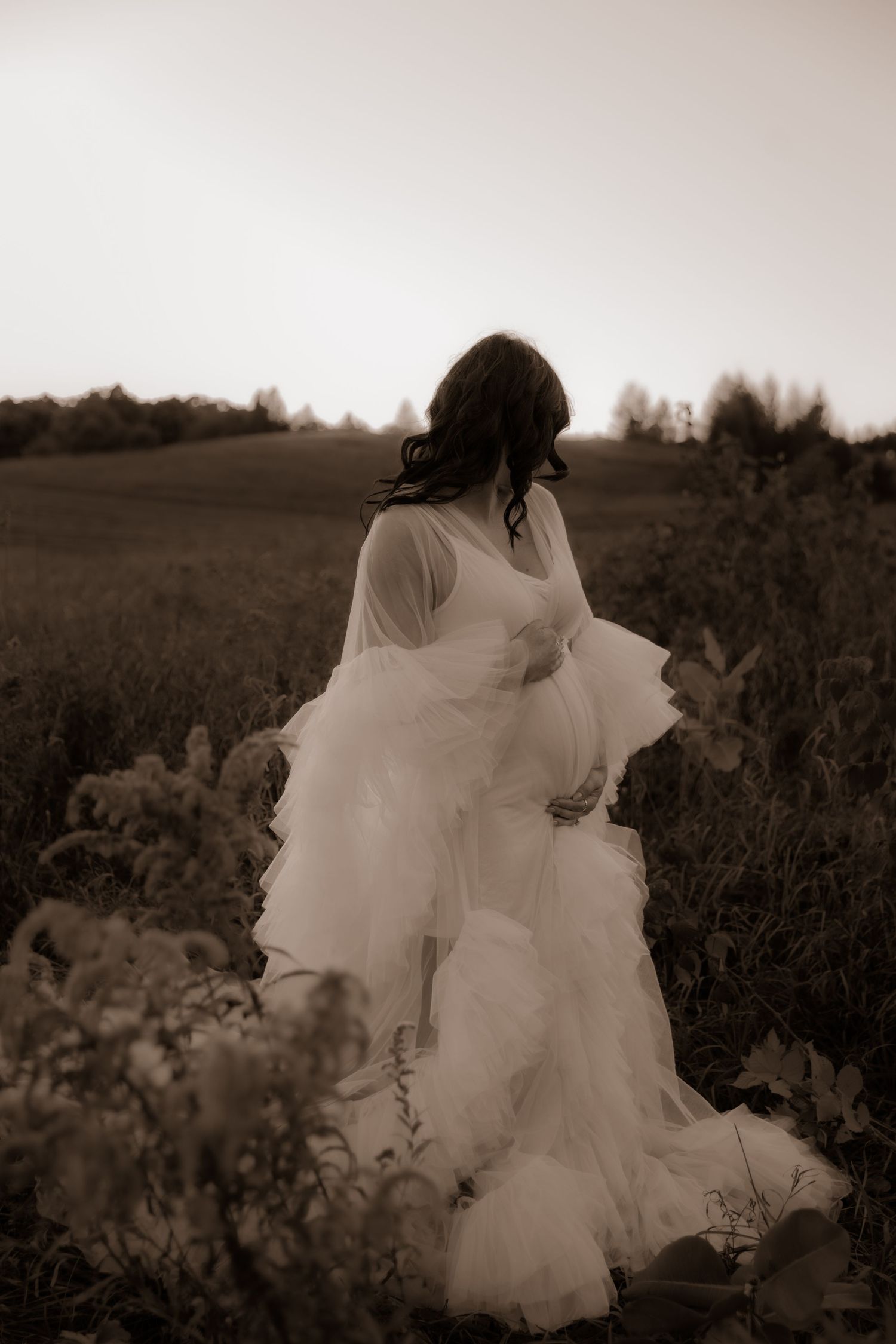 A figure in a flowing white dress stands in a sepia-toned field at dusk, creating a dreamy romantic silhouette.