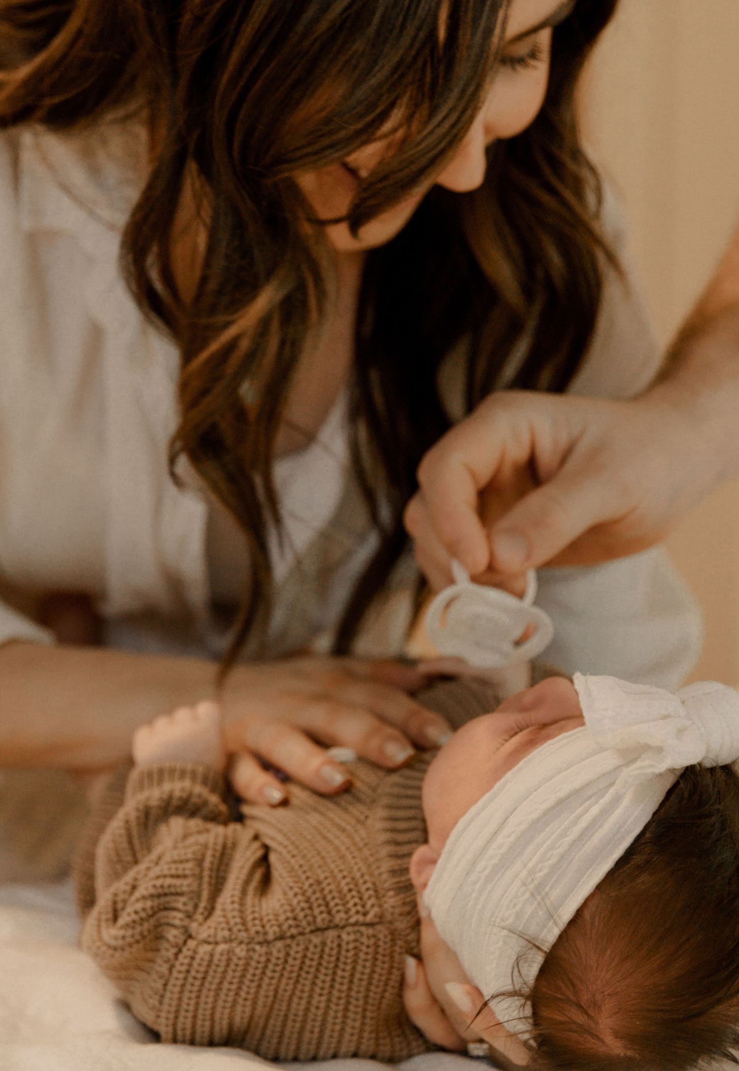 A tender moment showing gentle care and nurturing between parent and baby dressed in soft knitted clothing in warm lighting.