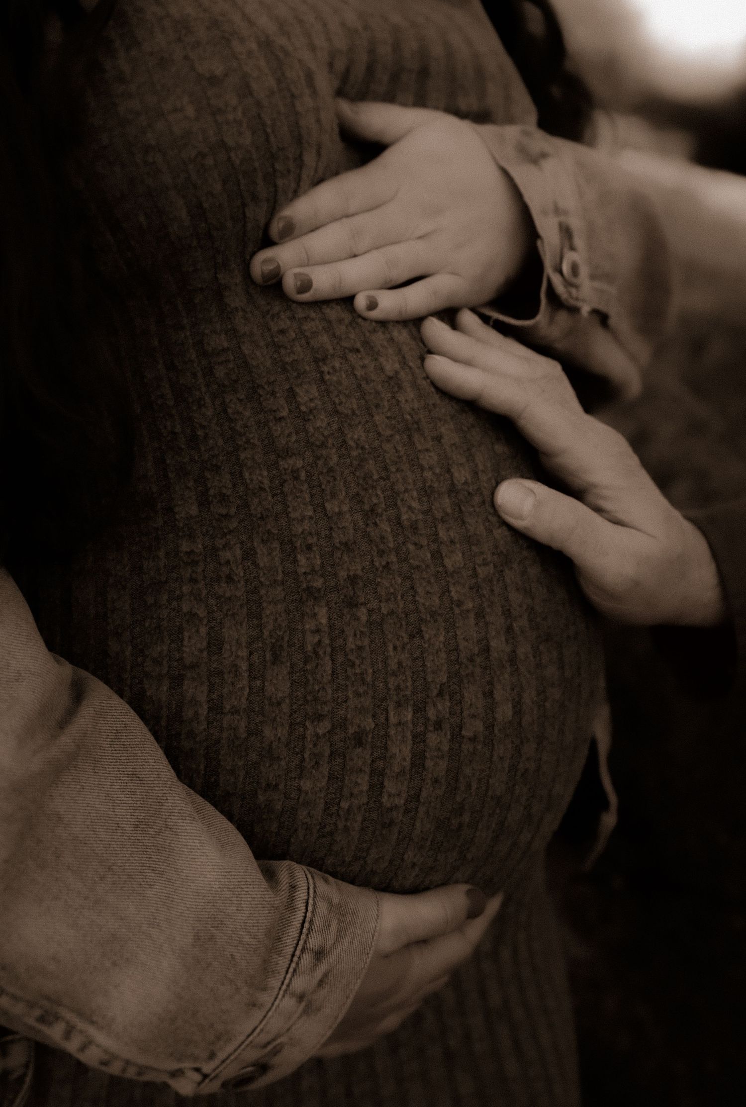 Small hands tenderly touch and explore a dark knitted sweater in a warm sepia-toned photograph.