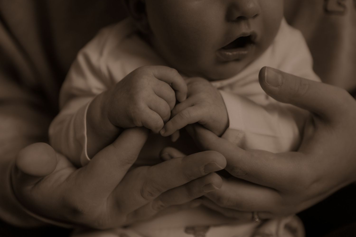 A close-up black and white shot of tiny infant hands being held by adult hands.