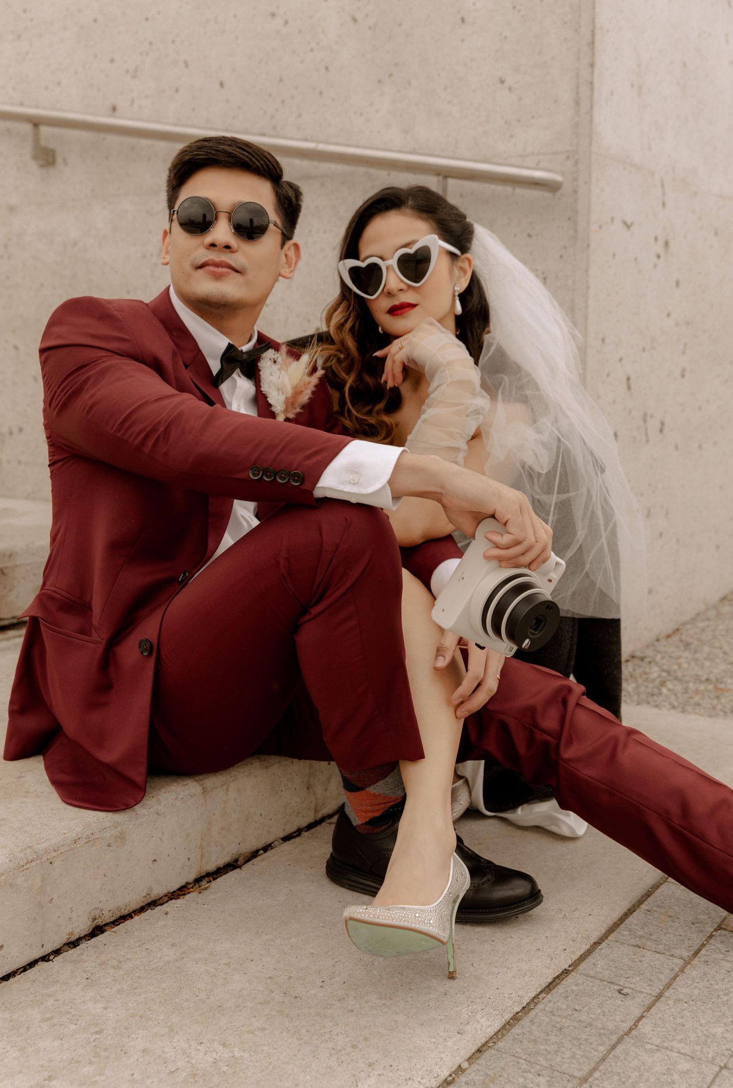Fashionable wedding couple in sunglasses pose casually on concrete steps.