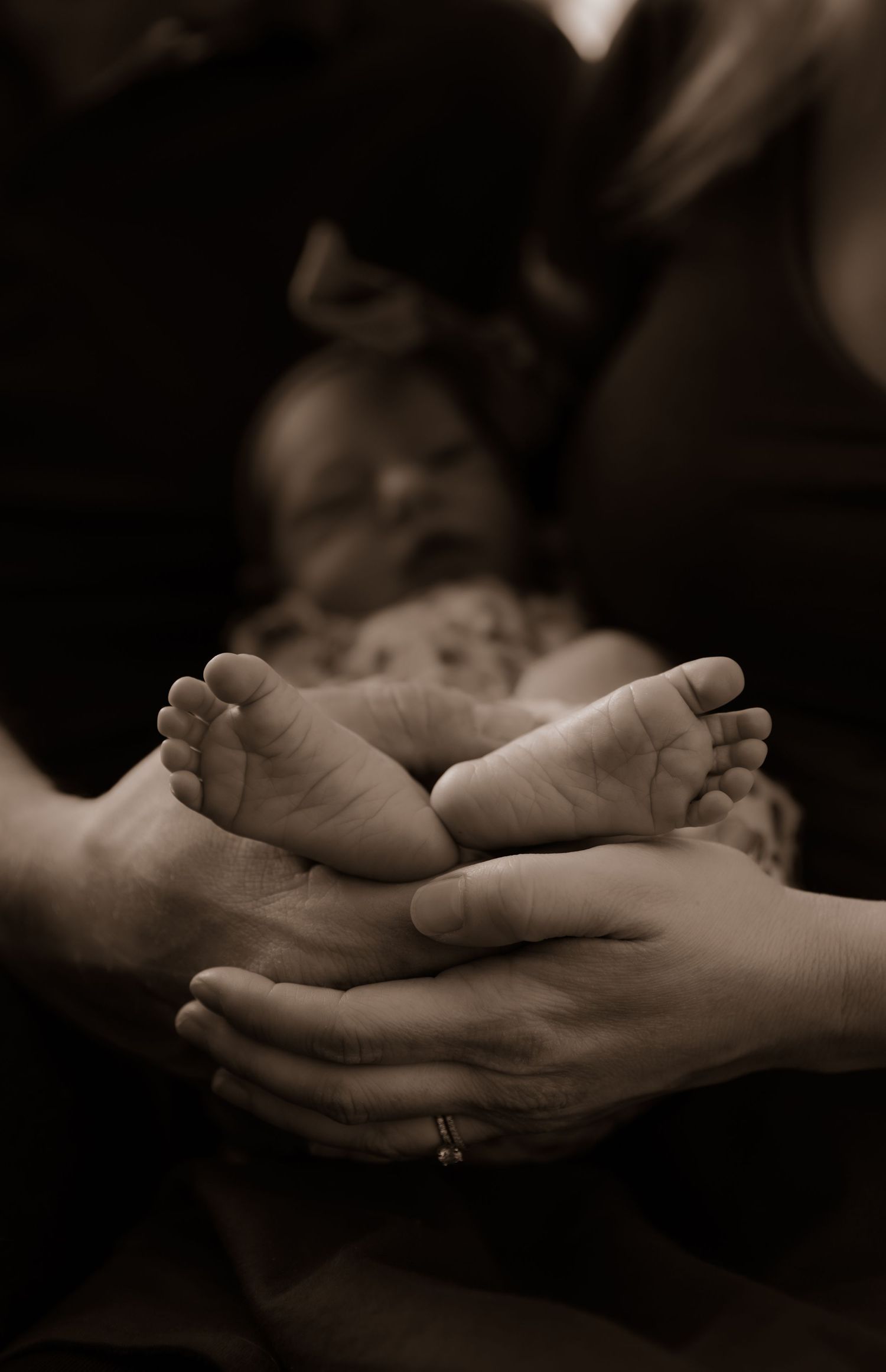 Tiny newborn feet cradled gently in adult hands, captured in sepia tones.