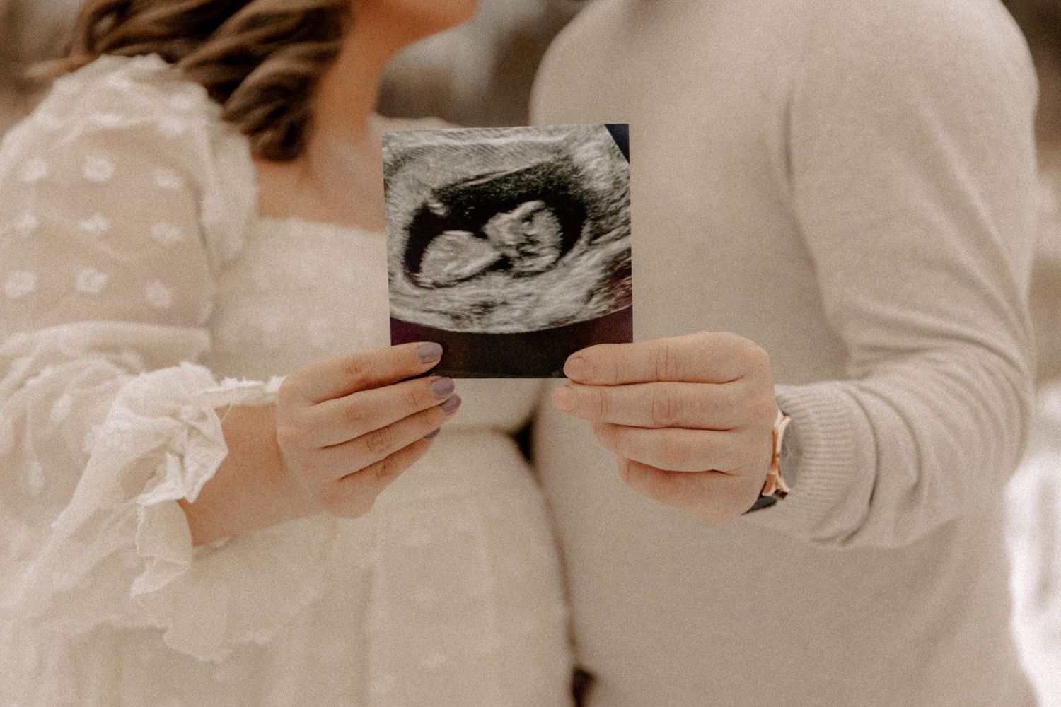 Someone holding an ultrasound photograph against a light background in a tender pregnancy announcement moment.