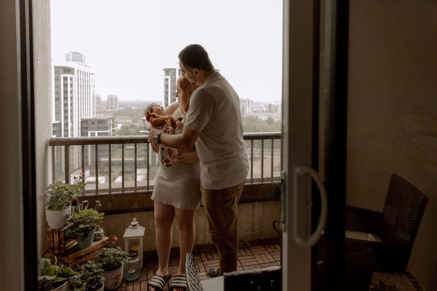 A couple shares an intimate moment on their apartment balcony overlooking a city skyline at dusk.