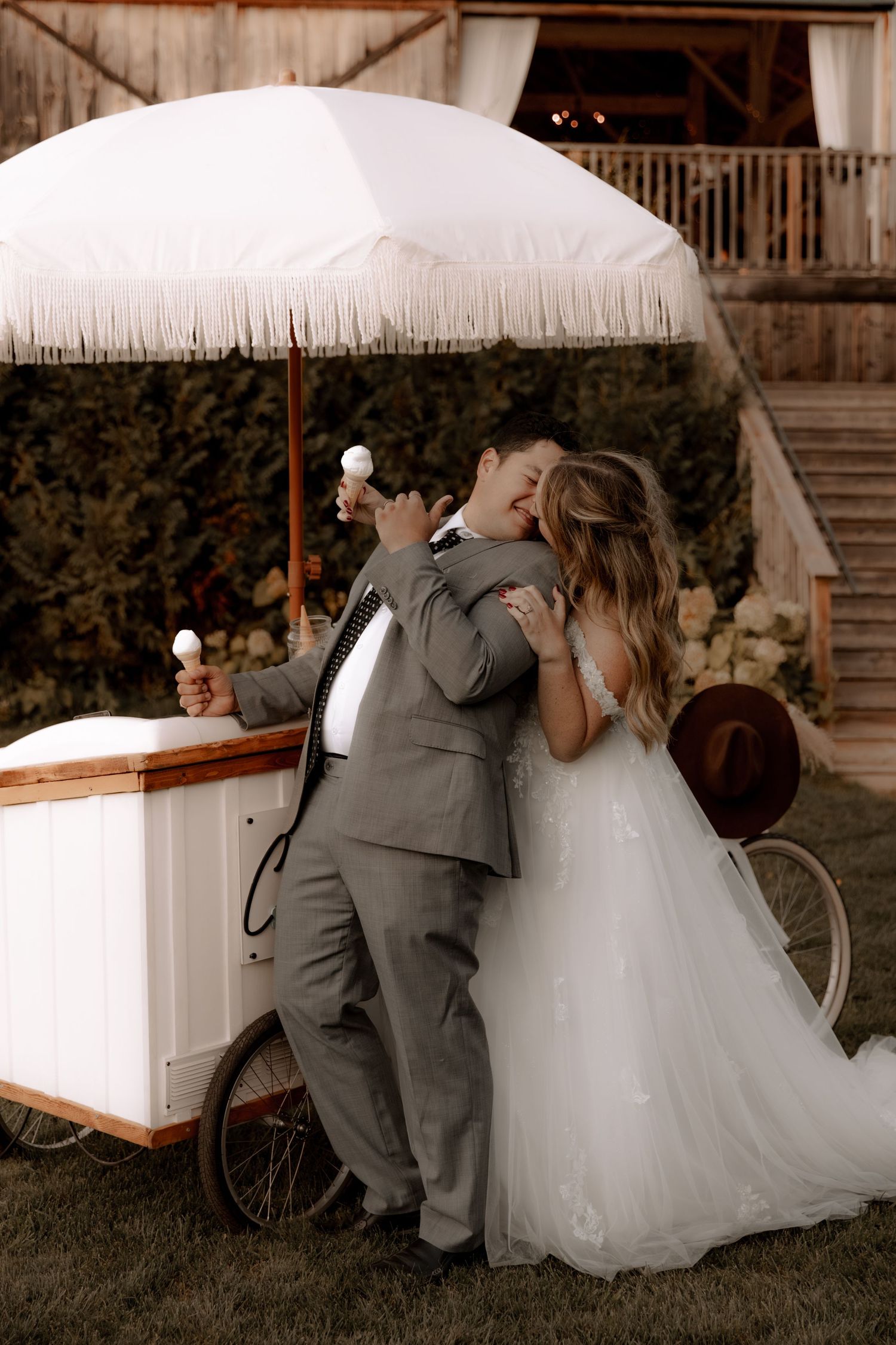 Newlyweds share a playful moment while getting ice cream from a vintage cart at their rustic wedding.