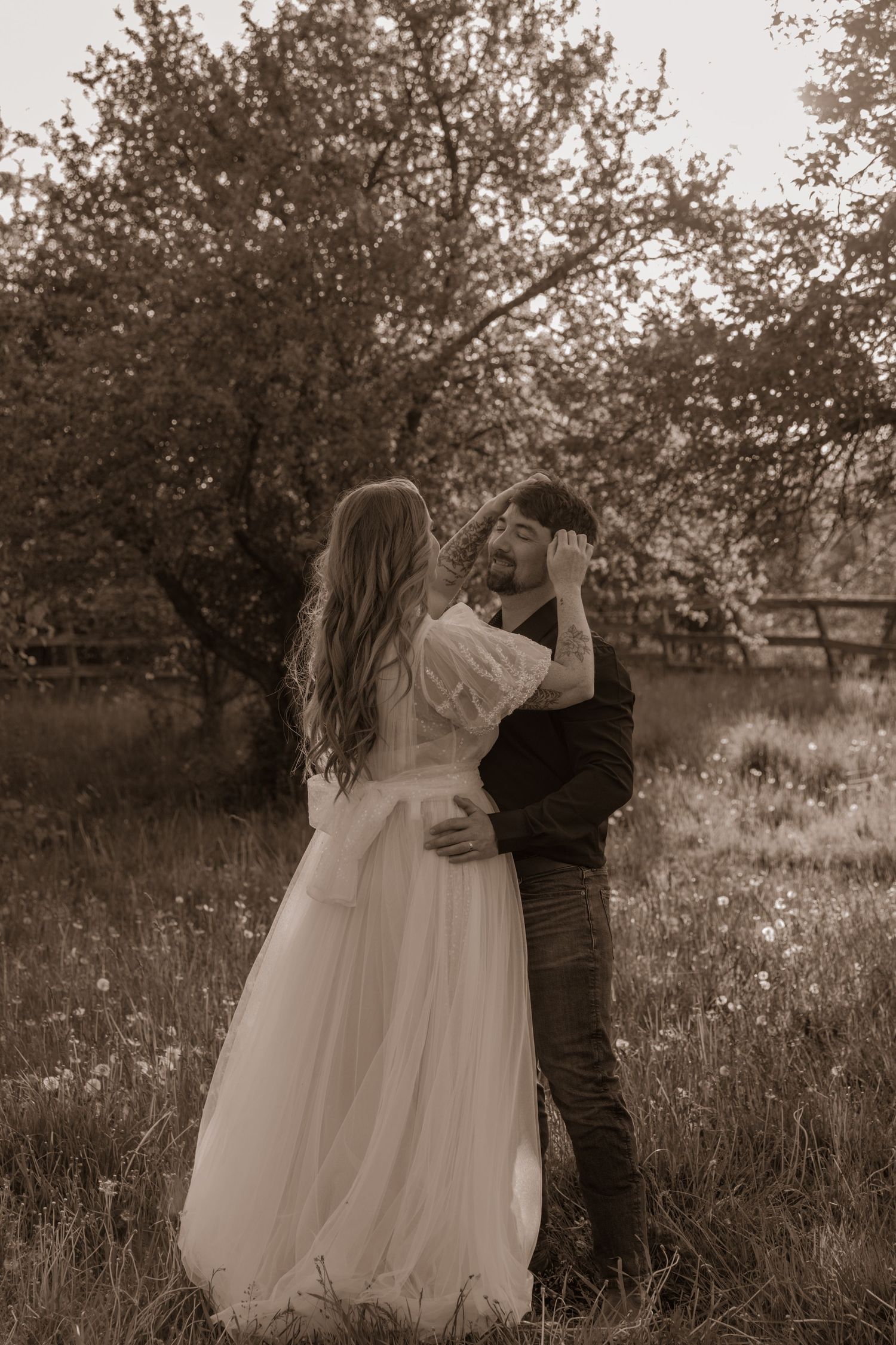 Intimate wedding portrait of a couple embracing in a meadow at sunset.