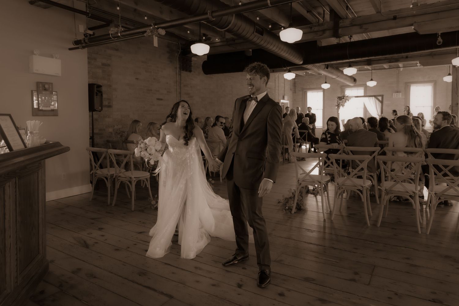 A romantic wedding scene captured in sepia showing a celebration in an industrial-style venue.
