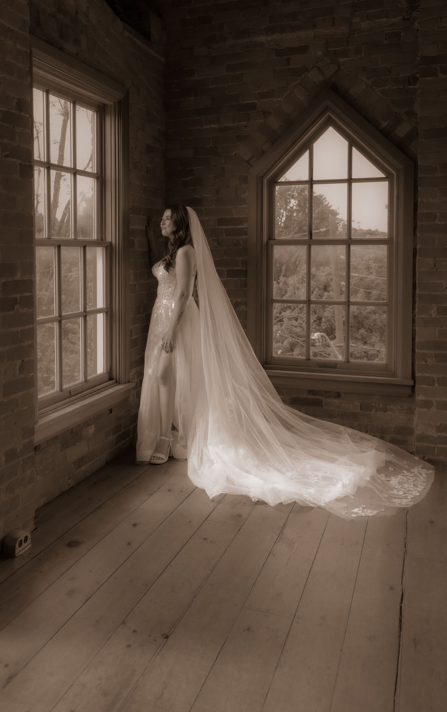 A dramatic bridal portrait in a rustic room with gothic windows and flowing veil.