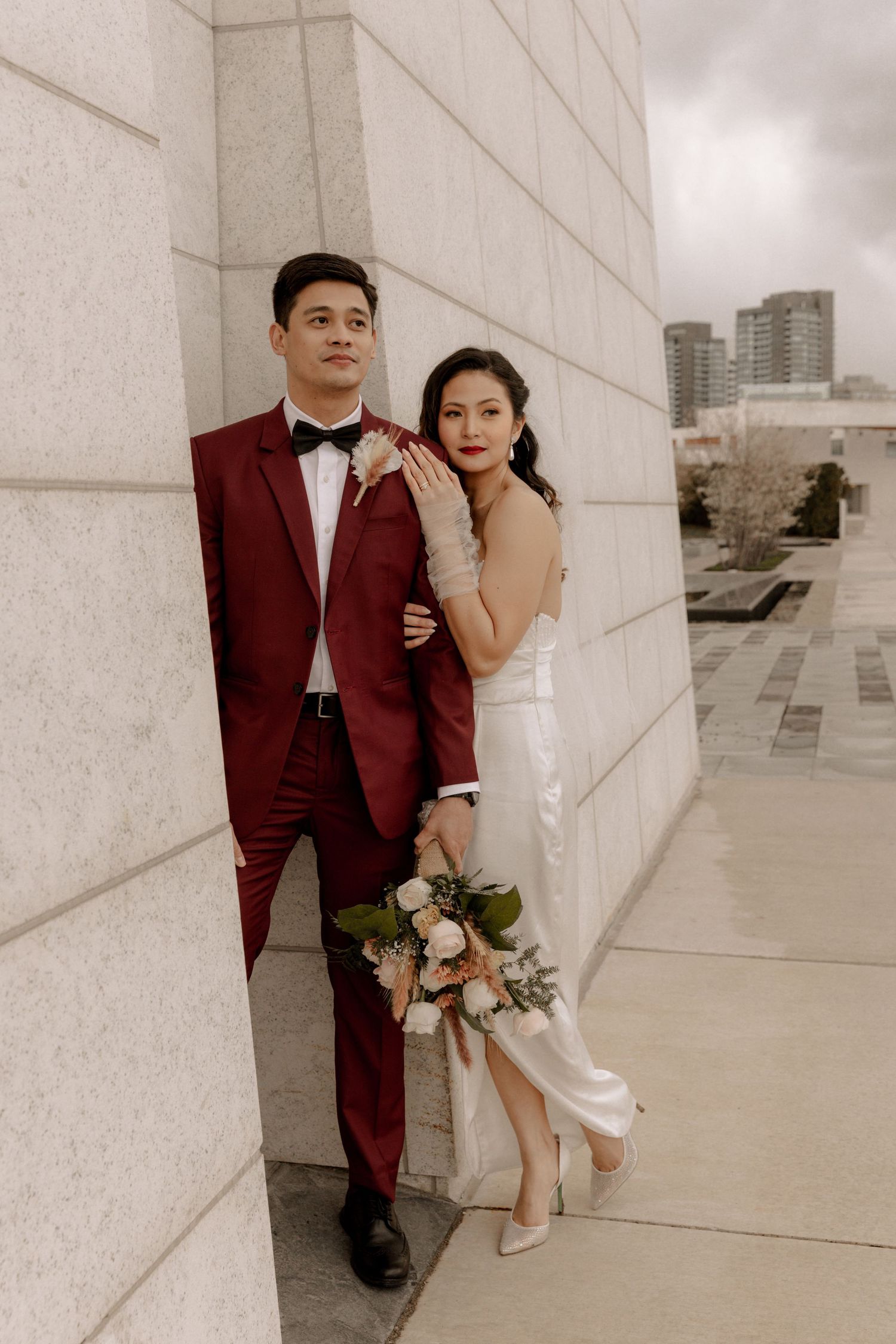 A stylish couple in formal wear poses against a modern architectural backdrop in the city.