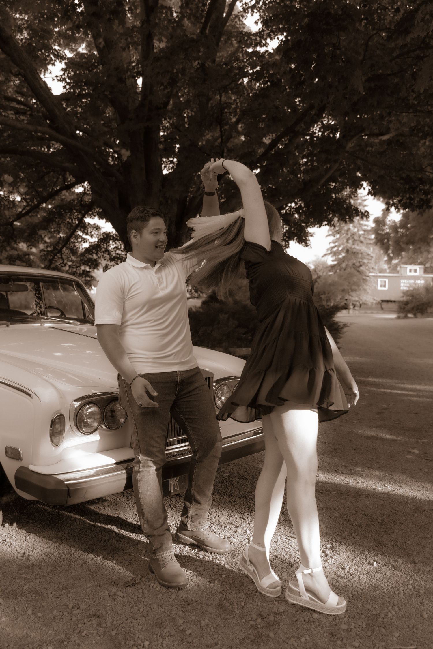 A couple poses playfully by a vintage car in a black and white photo.