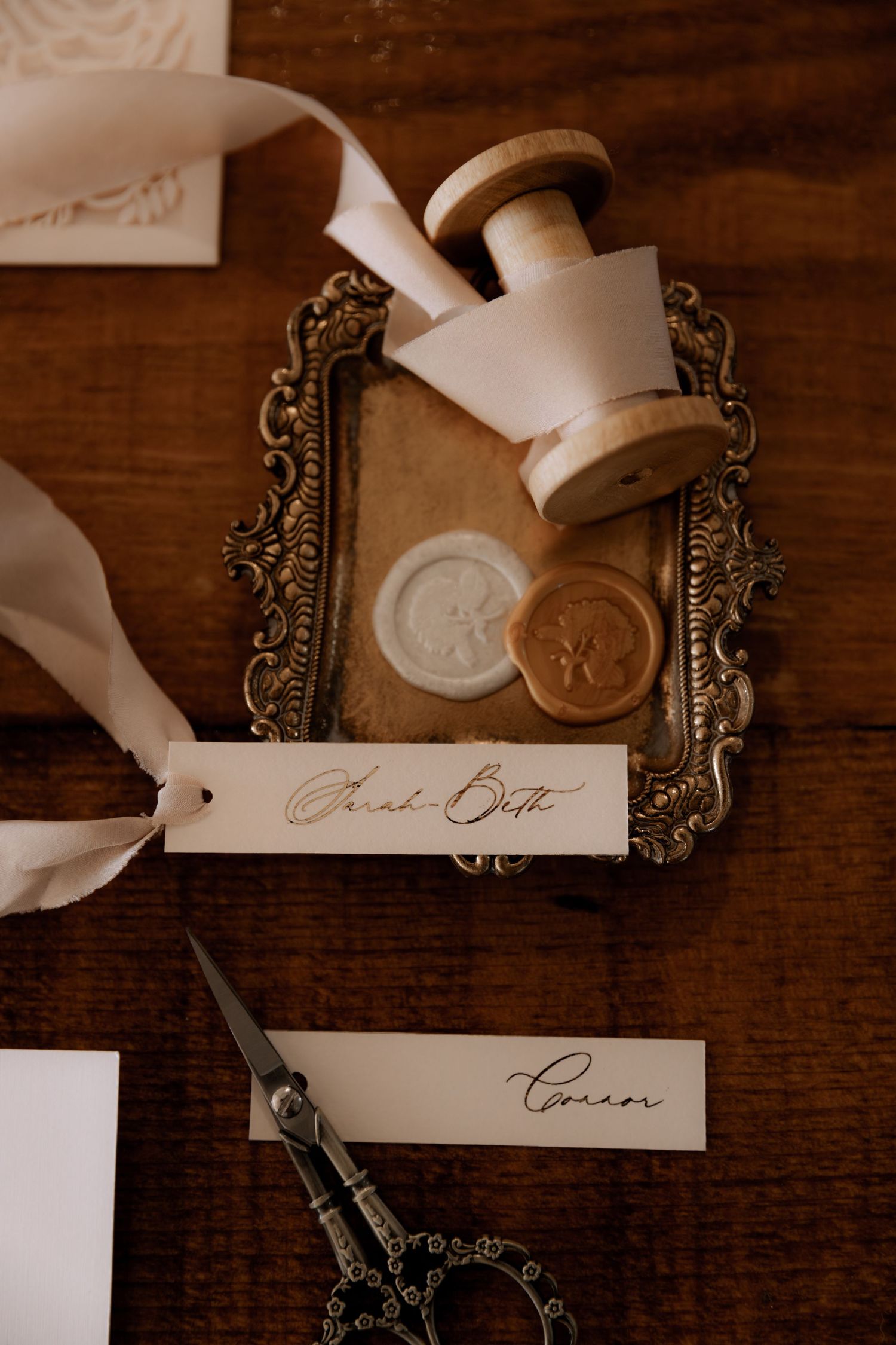 Vintage-style wax seal stamp and scissors with calligraphy name tags on ornate metal tray.