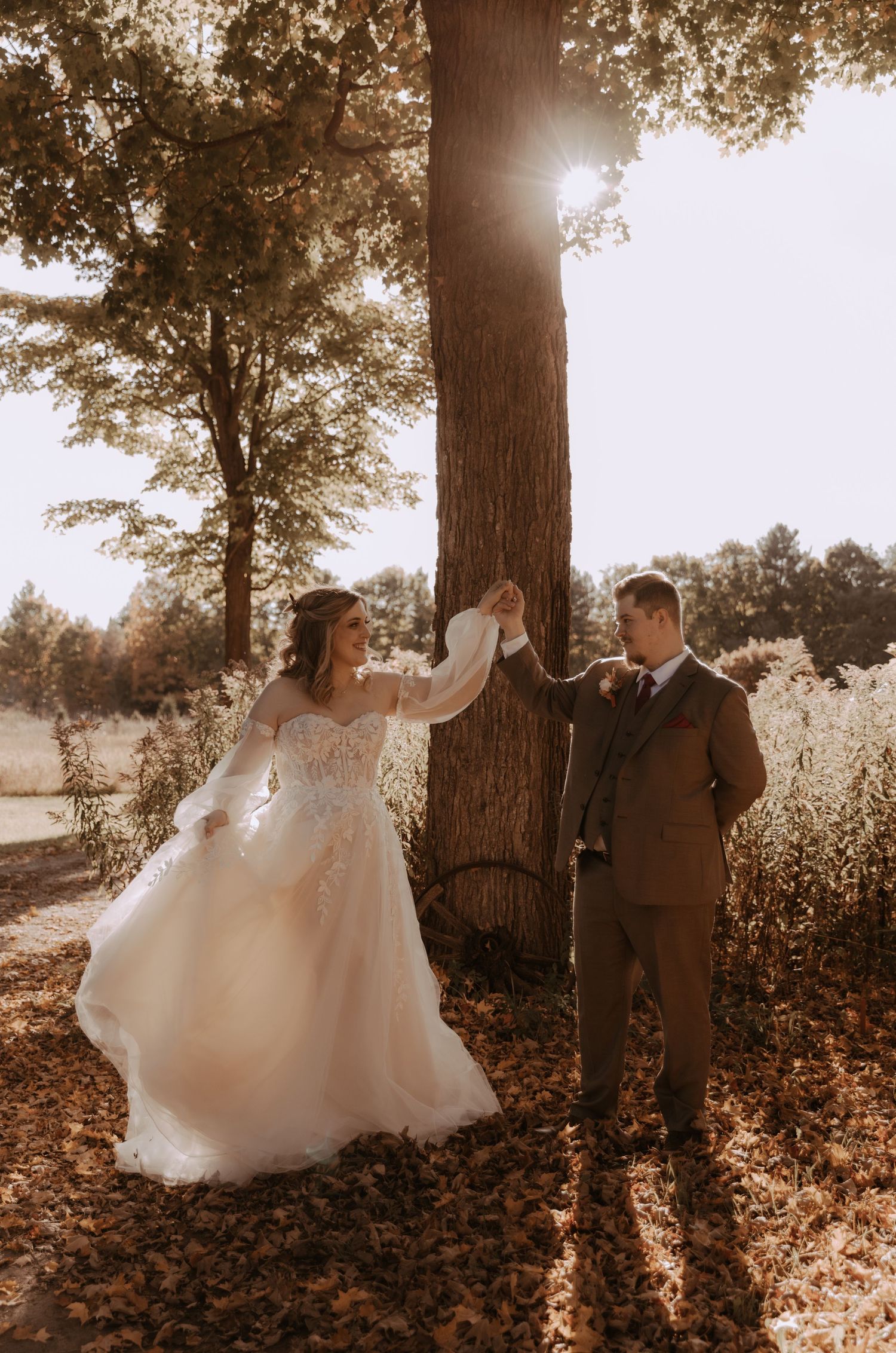 Couple sharing romantic moment under large tree with sunlight streaming through autumn leaves.