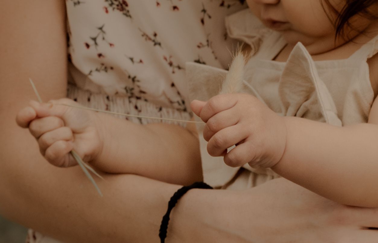Close-up detail of tiny hands working with thread against a soft sepia background.