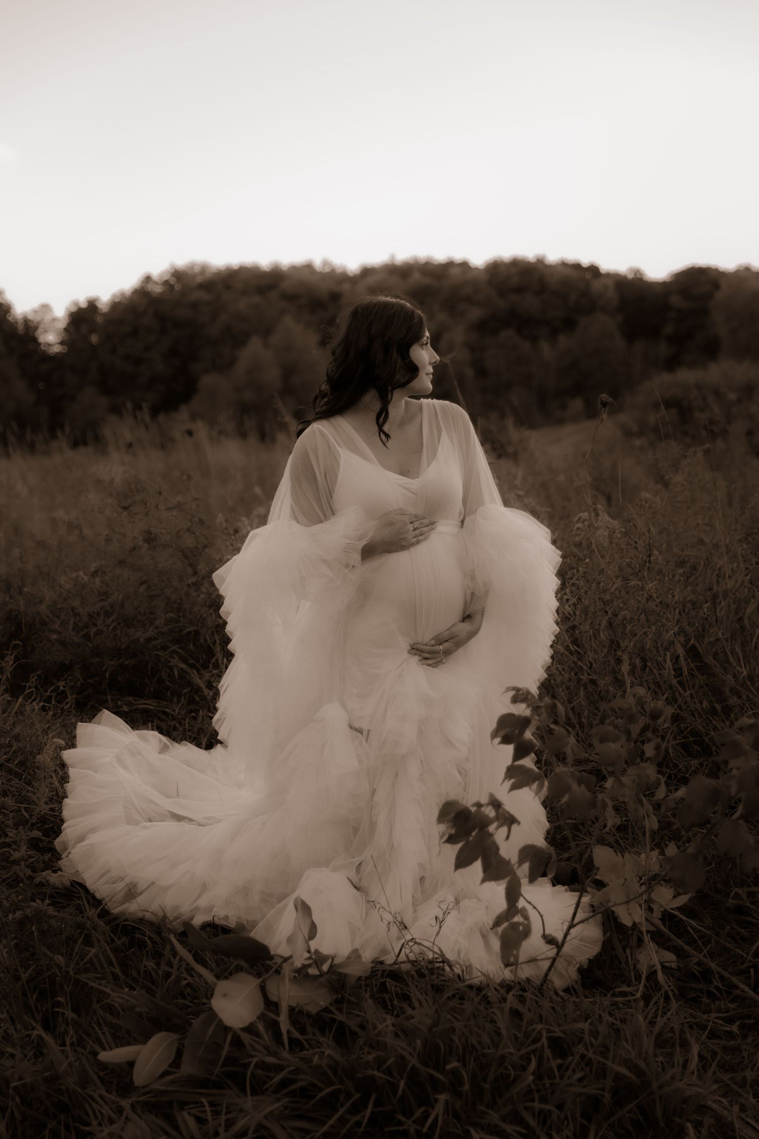 A dreamy sepia-toned portrait of someone in a flowing white dress standing in a wildflower field at dusk.