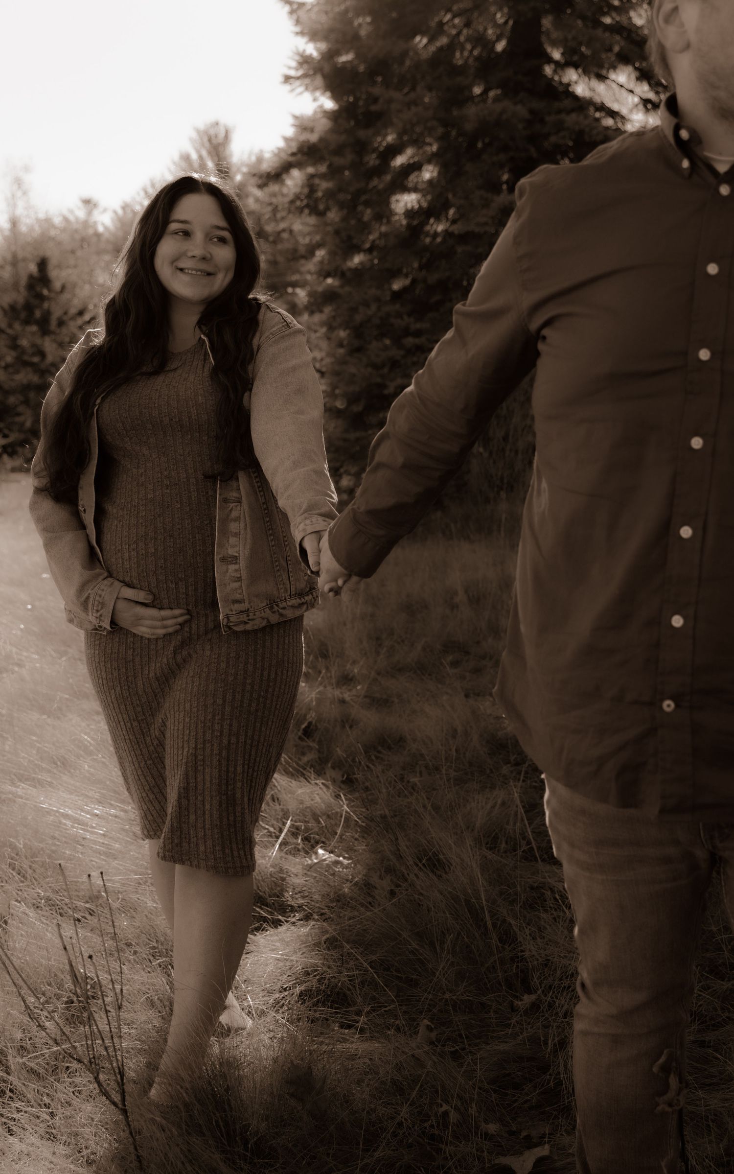 A sepia-toned photo shows a couple holding hands while walking outdoors along a path through natural vegetation.