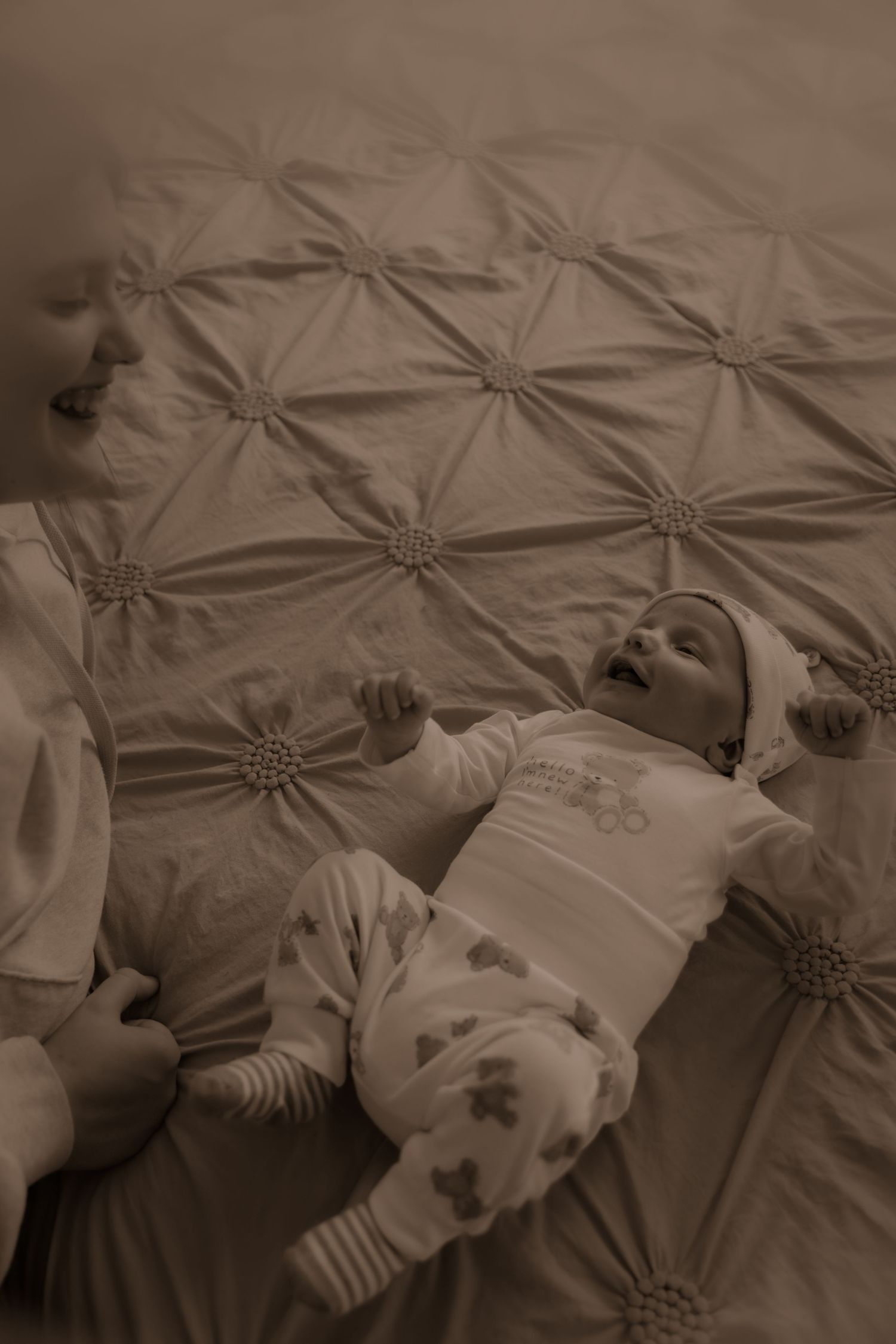 Sepia toned image of an infant lying on a tufted fabric surface wearing striped clothing and accessories.