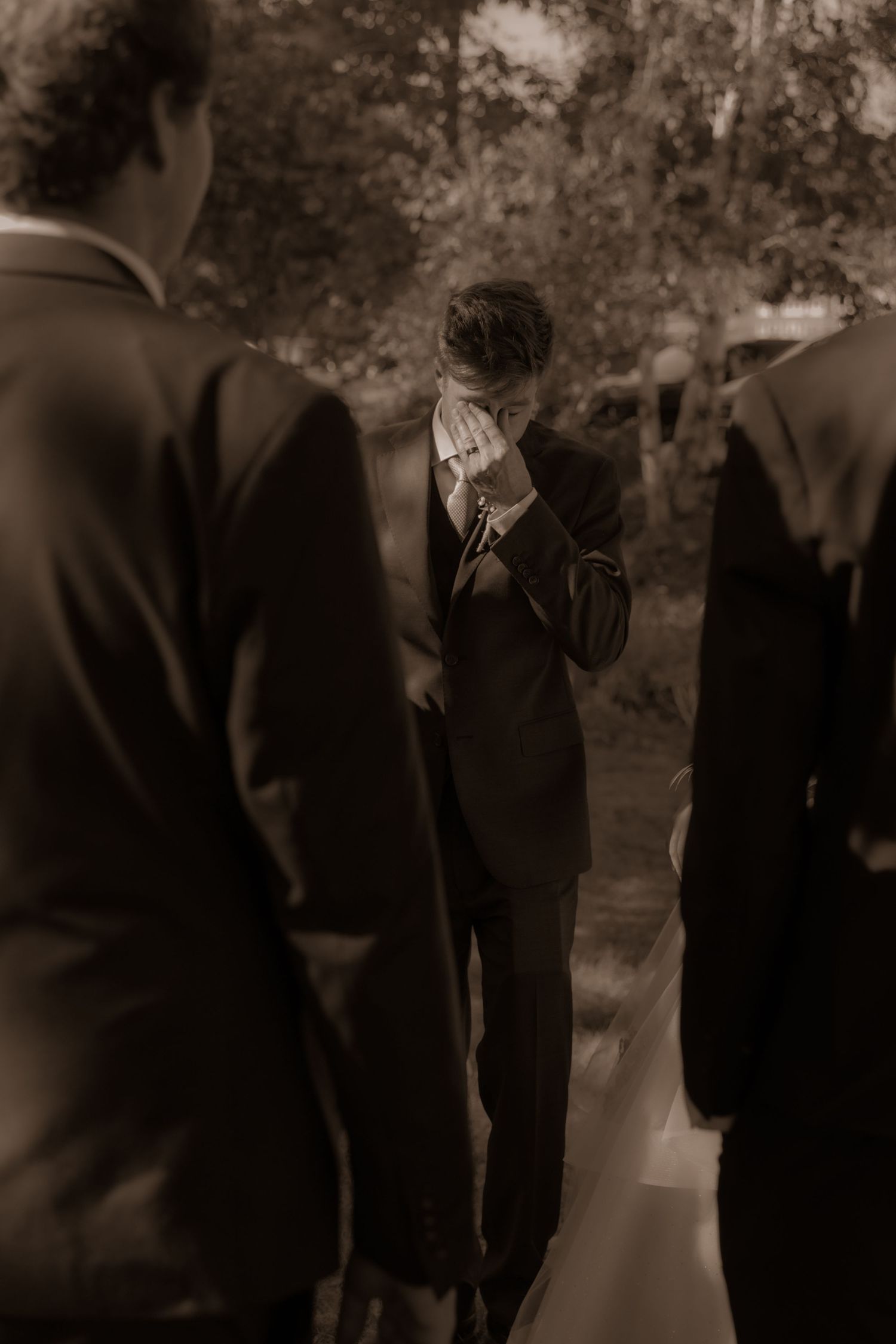 A sepia-toned candid moment between suited figures at an outdoor wedding.