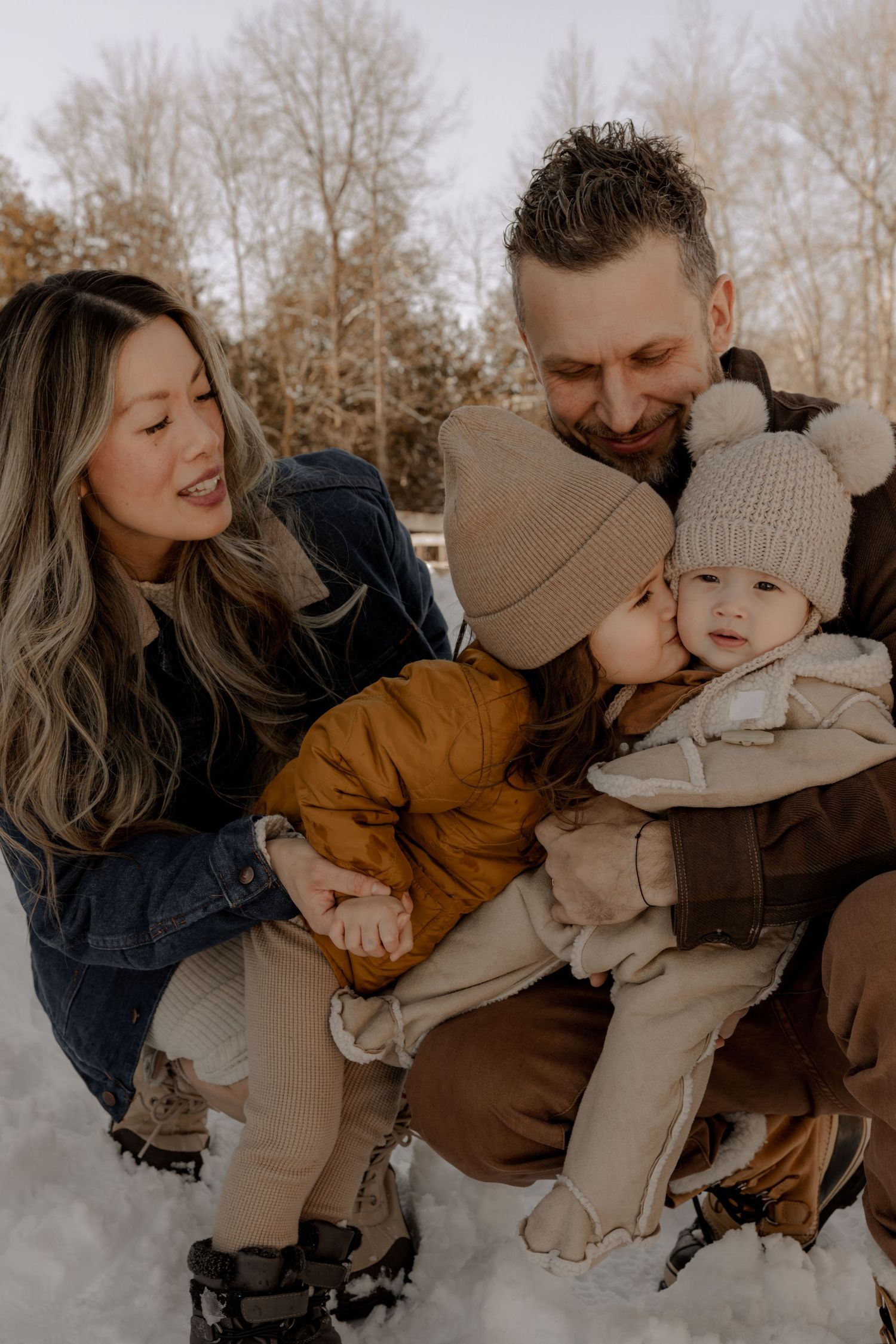 Family enjoying a playful moment together in the snow during winter while wearing cozy knitwear and outerwear.