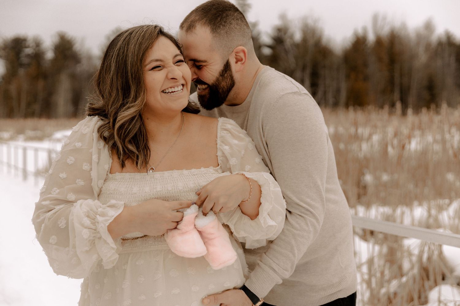 A couple embraces in a snowy winter field wearing neutral colored clothing during a romantic outdoor photoshoot.