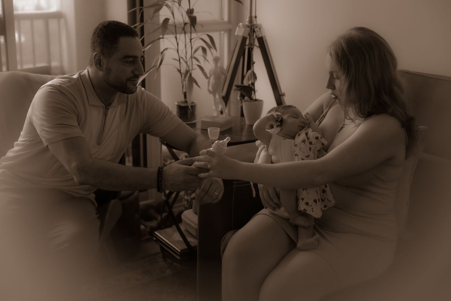 Sepia family portrait shows parents sharing precious moment with their baby in living room setting.