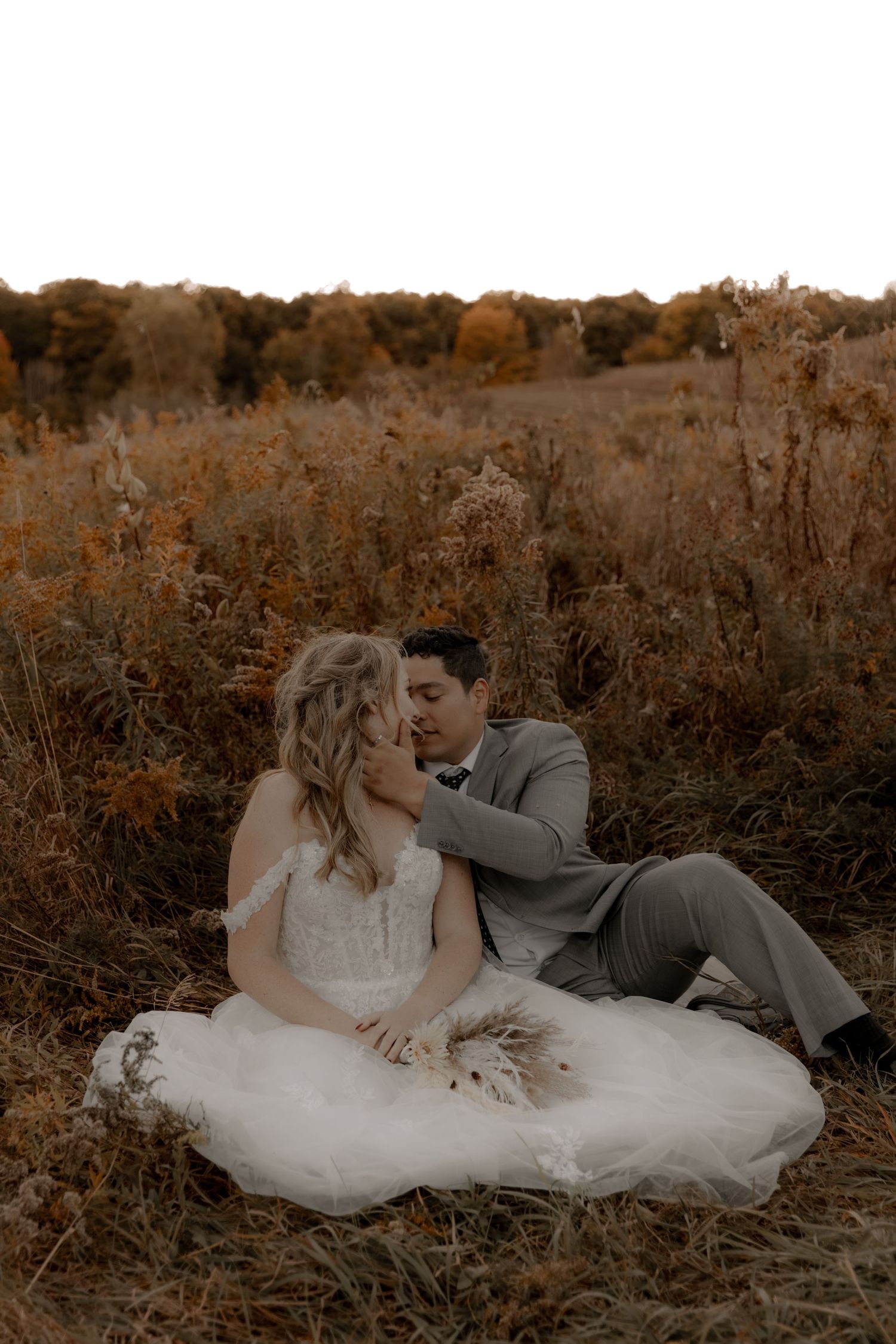 An intimate sepia wedding photo of a couple sharing a moment in a fall field.