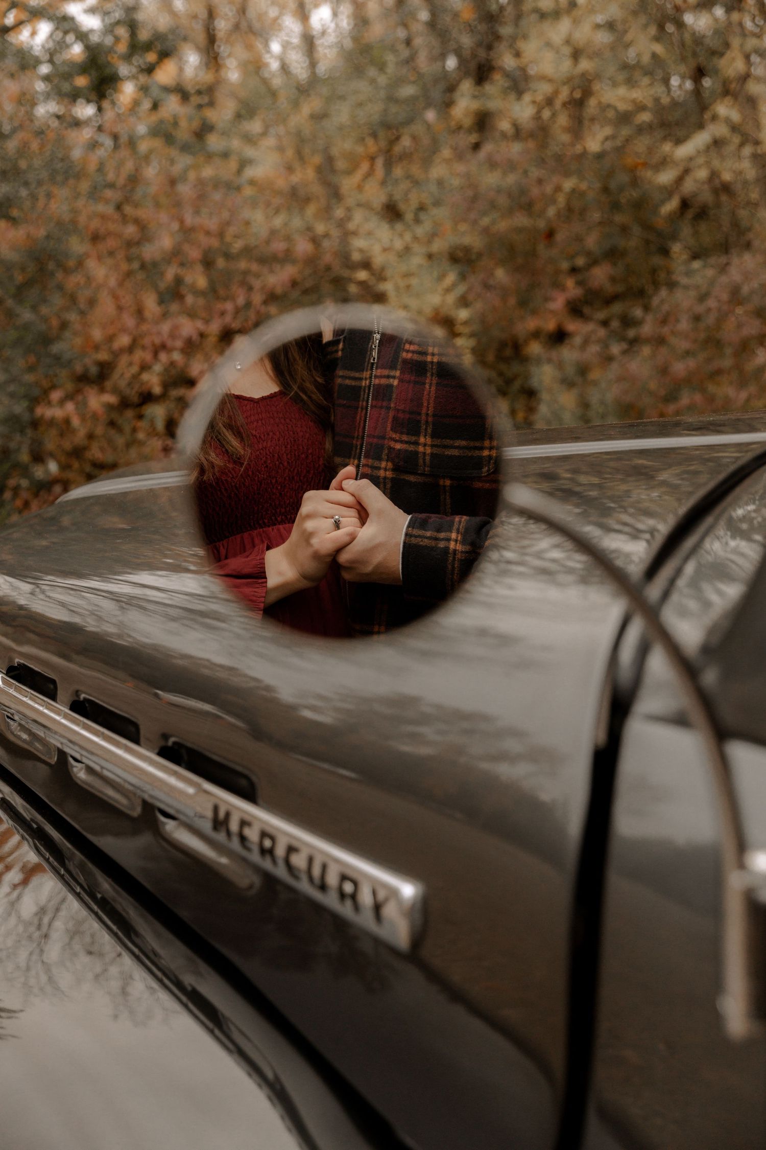A reflection in a vintage Mercury car's side mirror shows a romantic moment.
