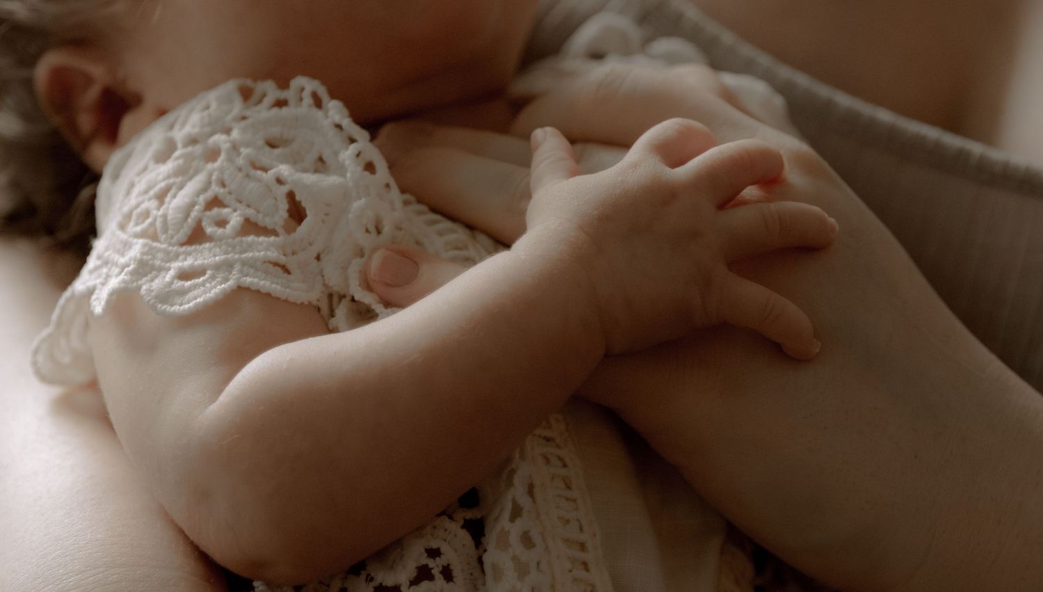 Close-up of a tiny baby hand clutching lace fabric in soft natural lighting.