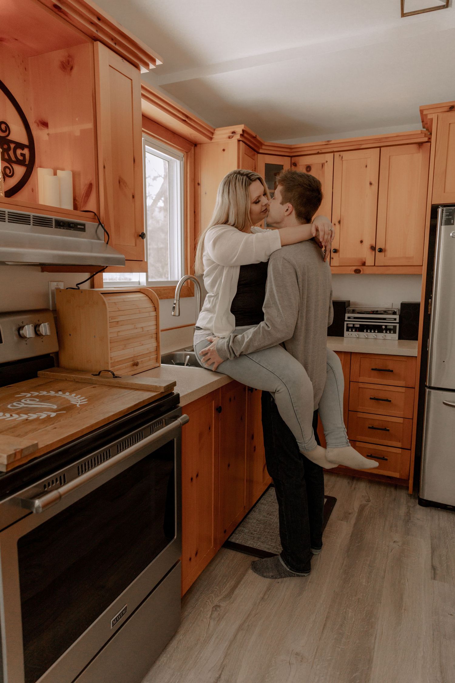 A couple shares an intimate moment in a cozy kitchen with warm wooden cabinets and modern appliances.