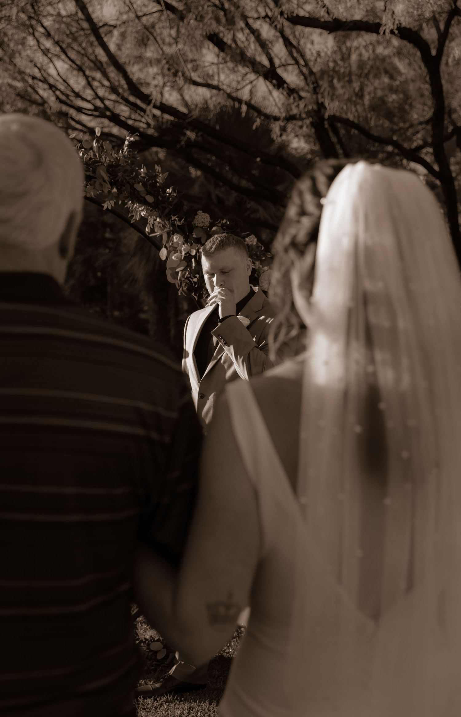 A wedding ceremony moment captured in sepia tones under tree branches.