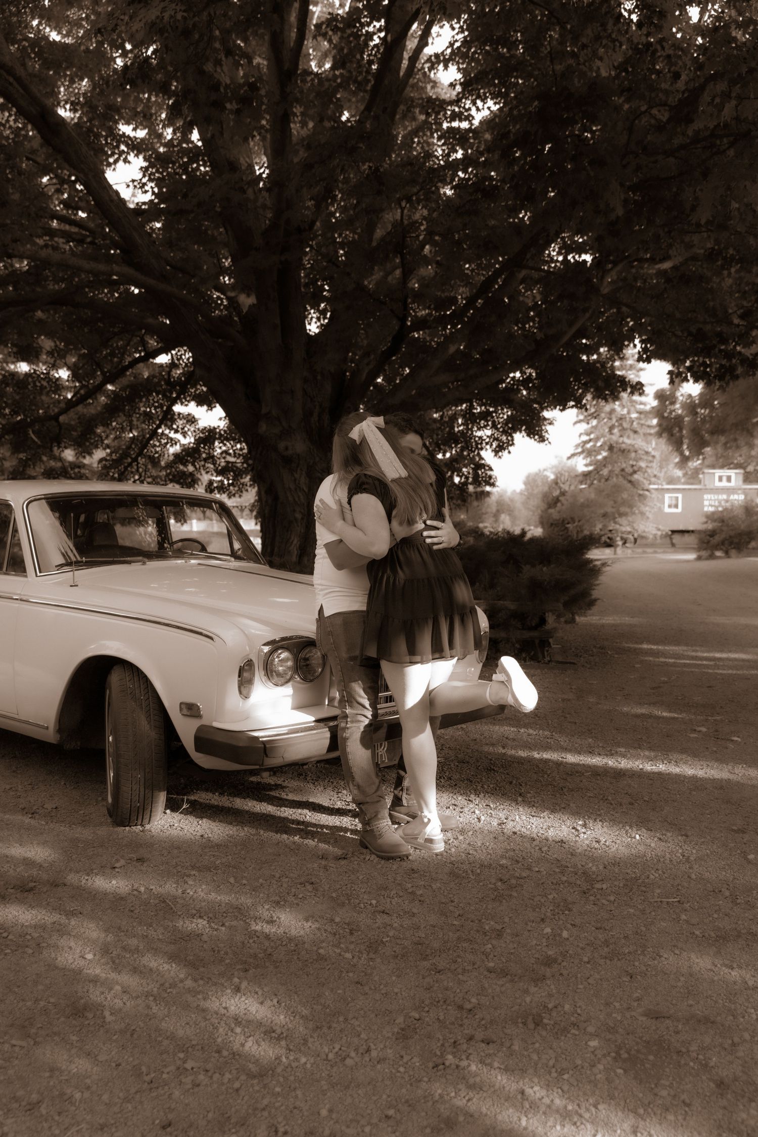 A romantic scene beside a classic car under a large tree in sepia tones.
