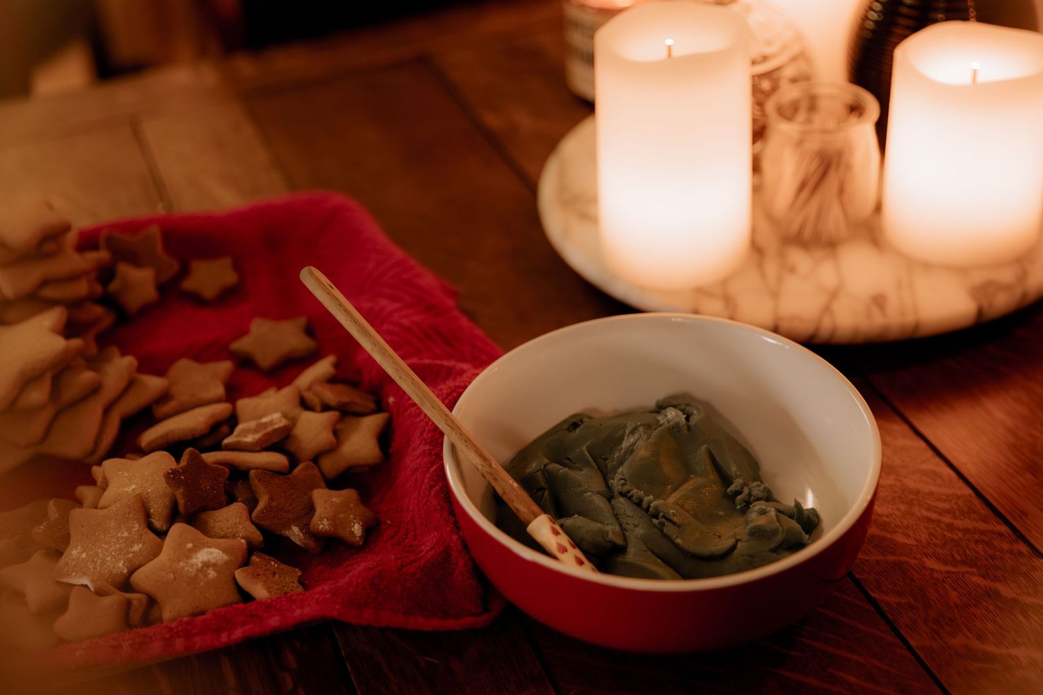 A bowl of food illuminated by candlelight with snacks on a red cloth.