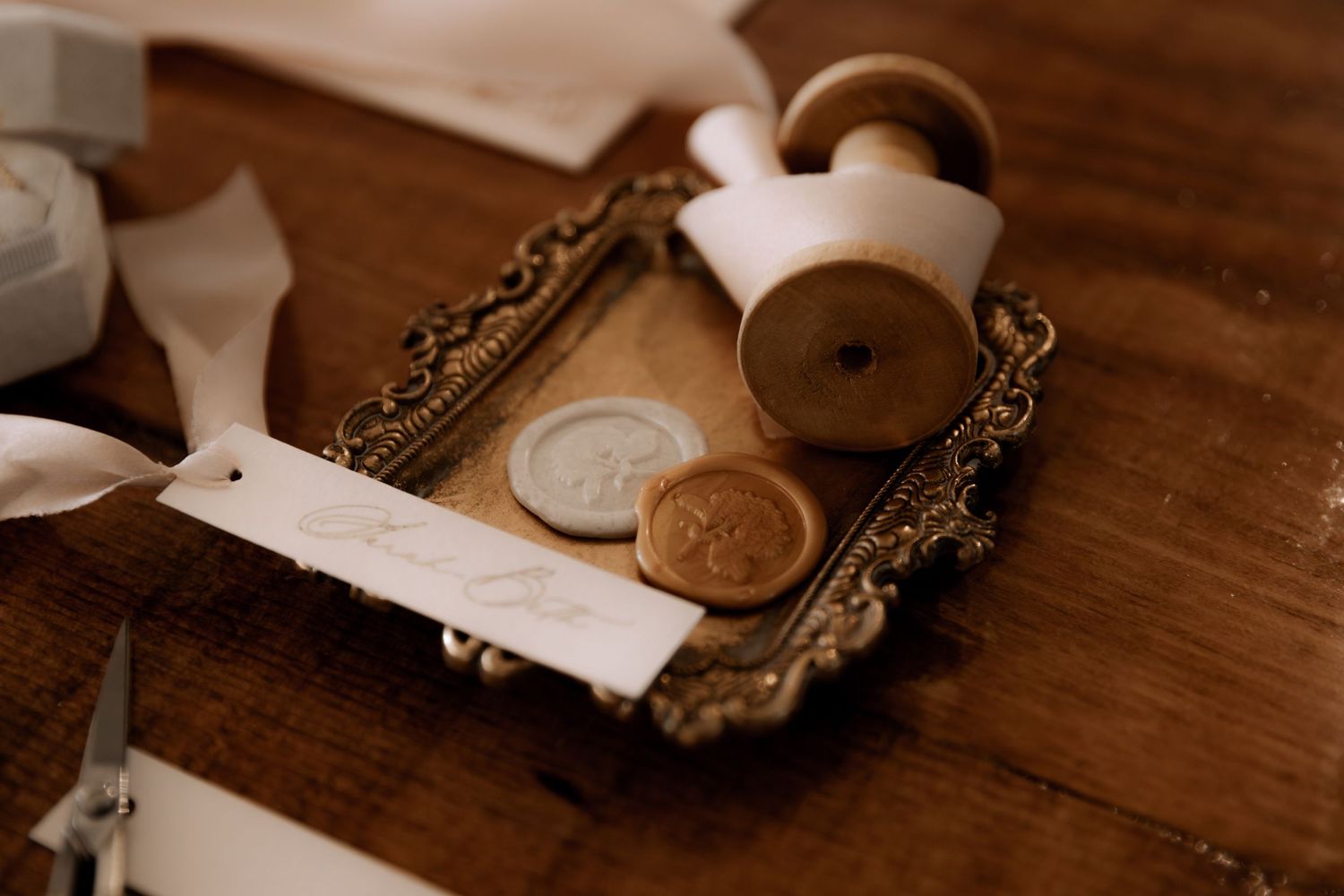 Antique brass tray containing wax seal stamps and delicate ribbon in warm sepia tones.