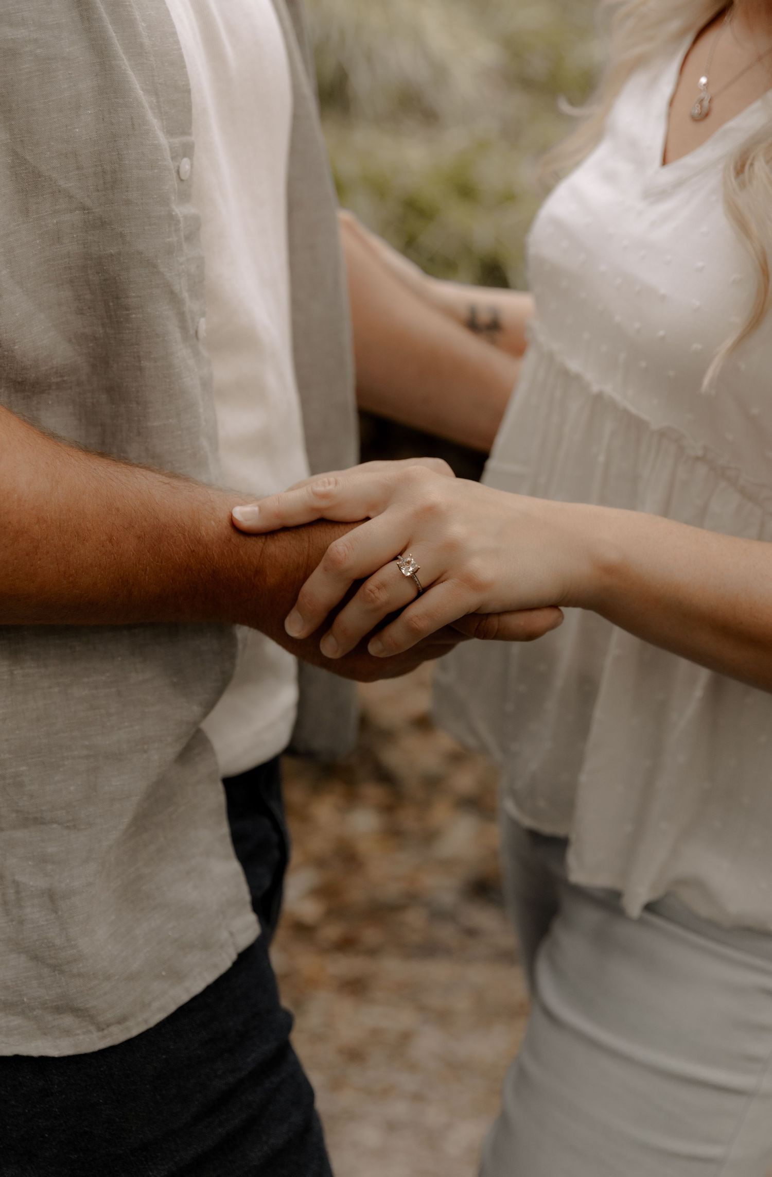 Intimate close-up of hands touching with engagement ring visible in soft natural light.