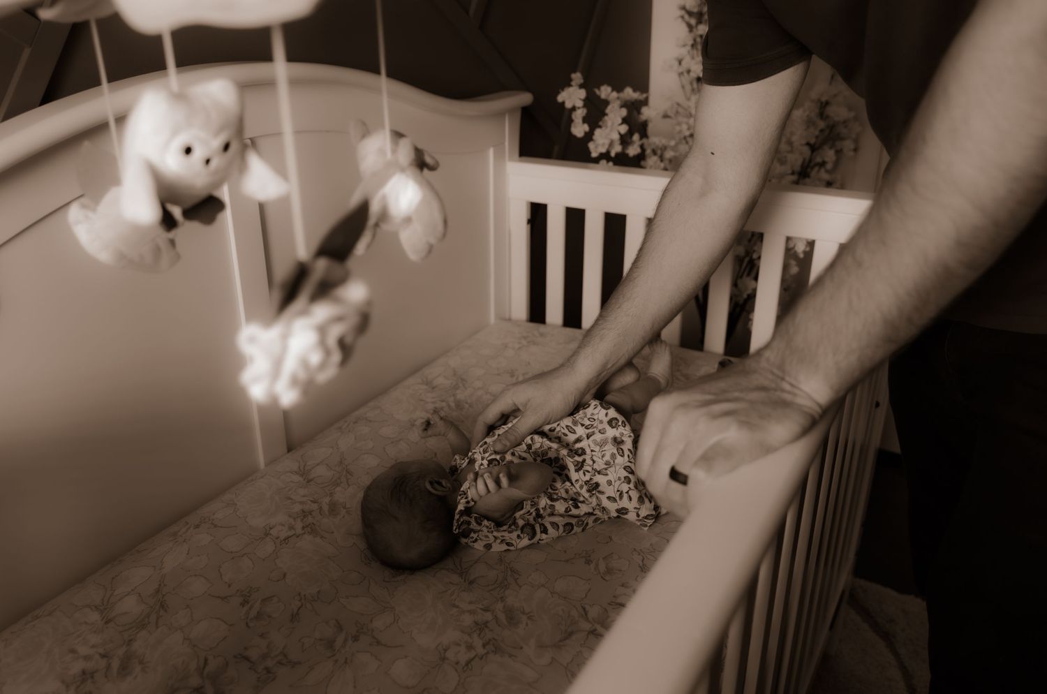 Sepia-toned nursery scene with stuffed animals hanging from a mobile over a crib.
