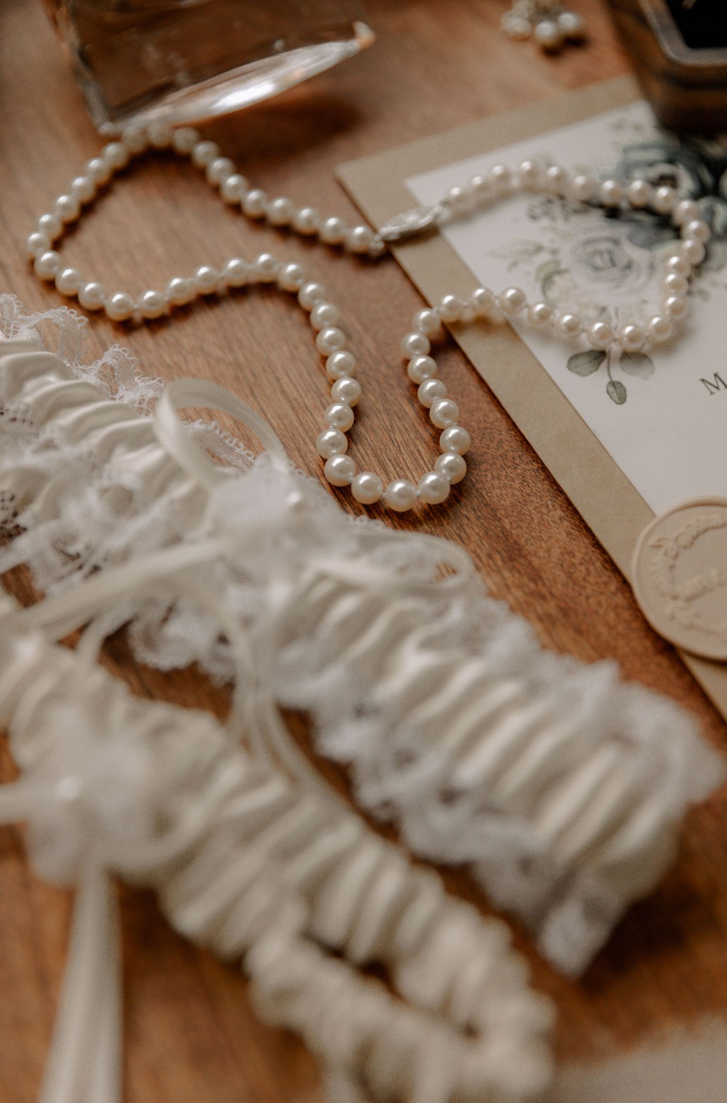 An elegant pearl necklace displayed with lace wedding accessories on a wooden surface.