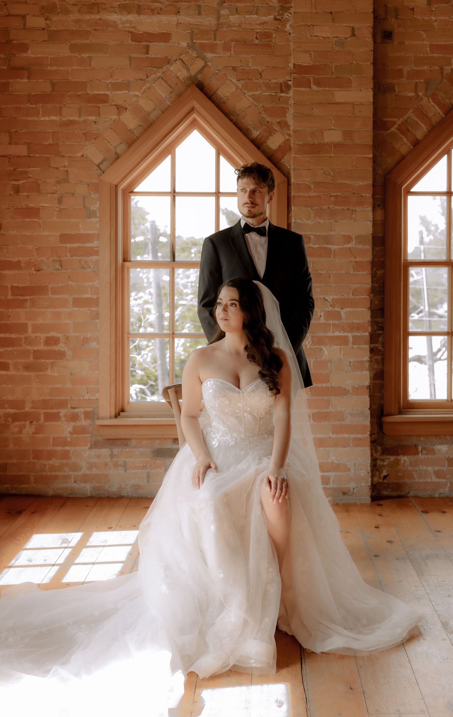 A sunlit portrait in a brick room with arched windows.