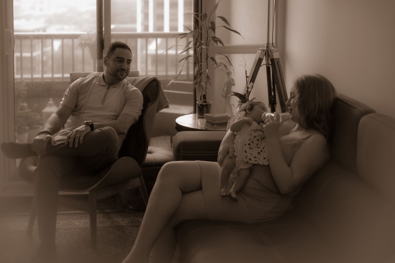 Three people relax in a modern living room with soft sepia tones and warm ambient lighting.