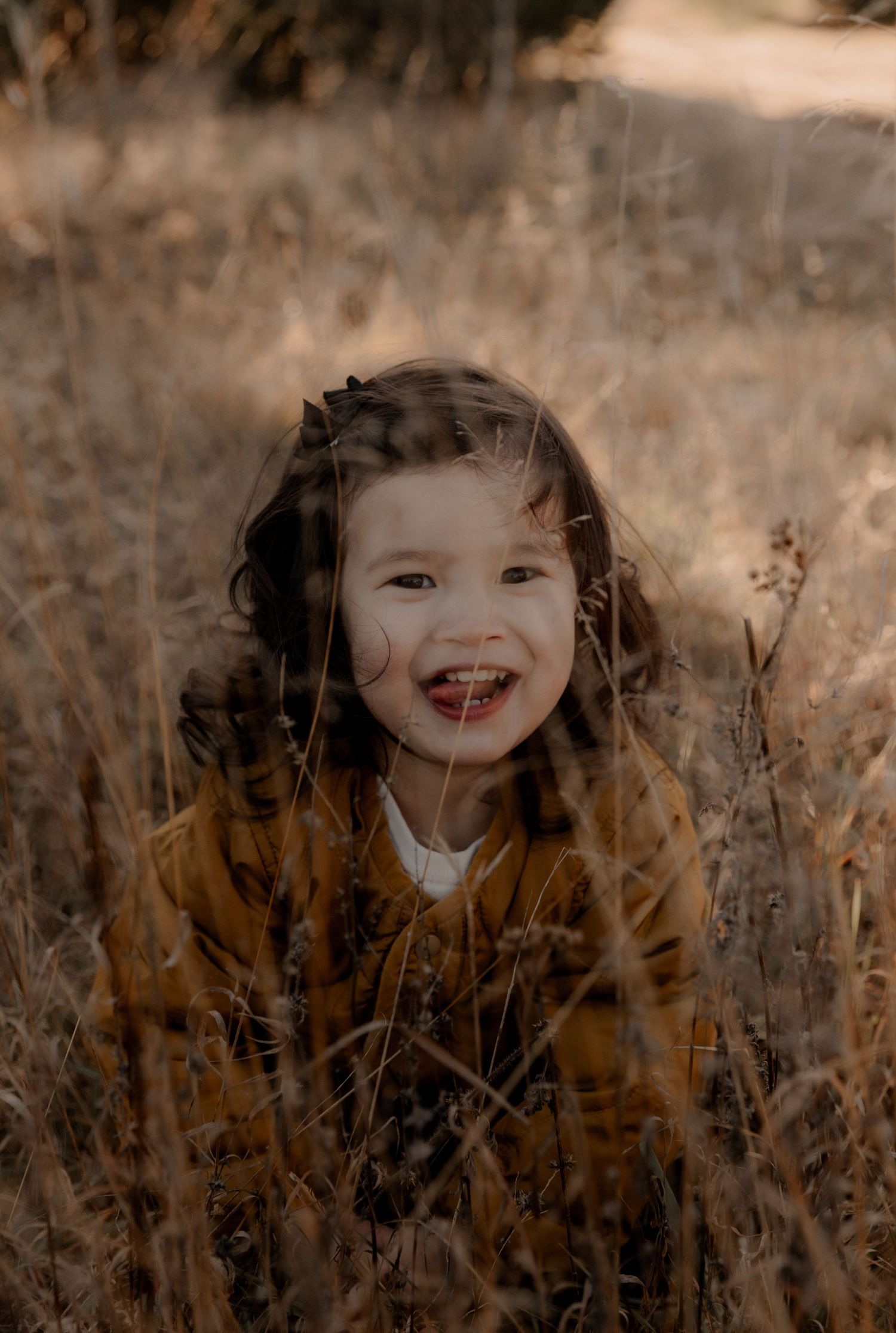 A joyful smile shines through tall autumn grass on a sunny afternoon.