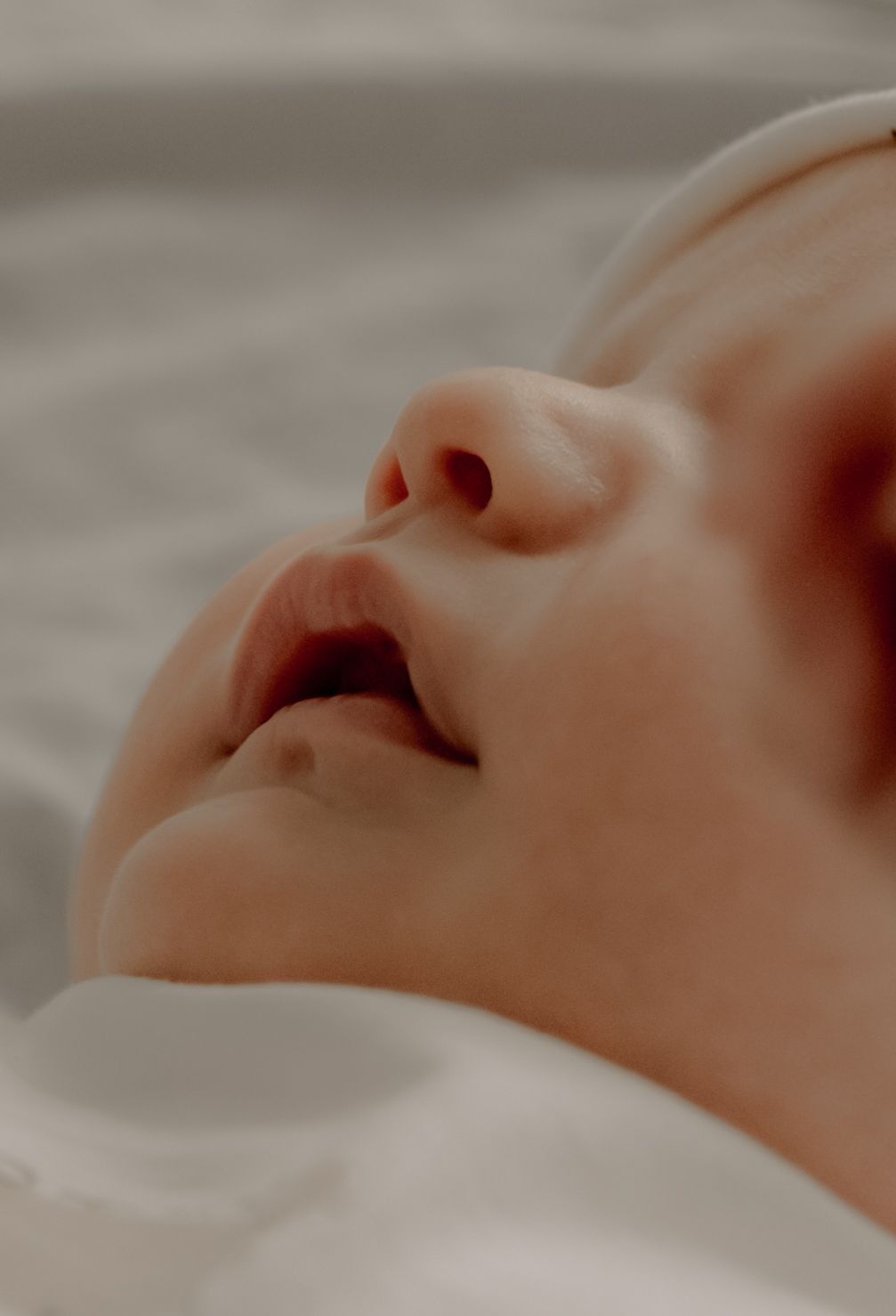 Close-up view of a sleeping baby's face showing peaceful expression against soft white bedding.