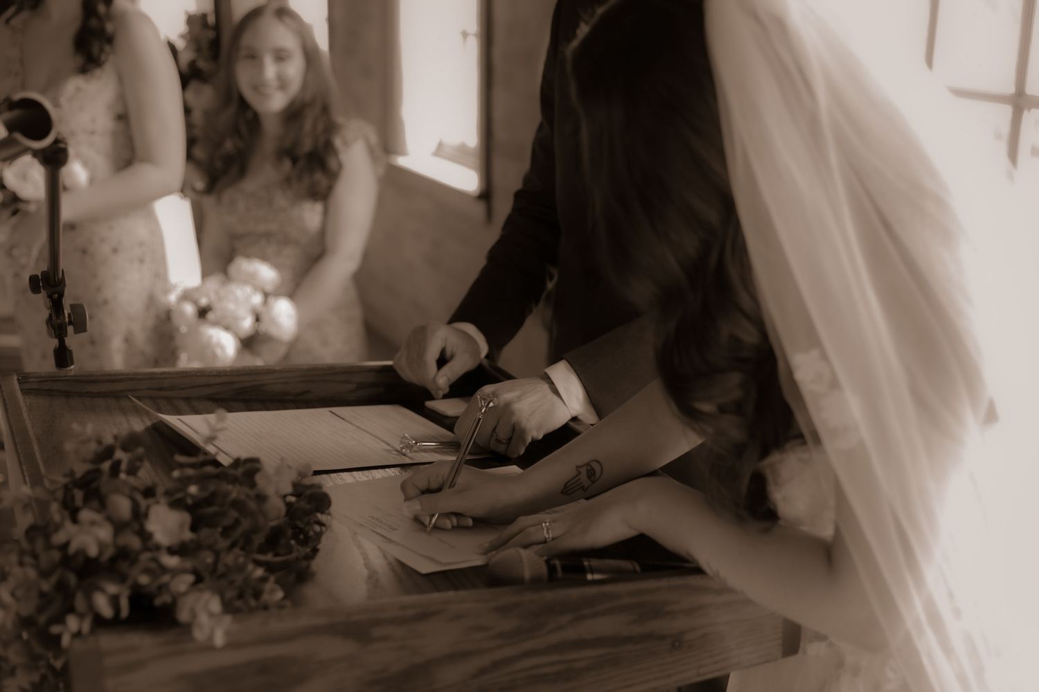 A wedding guest book signing moment captured in sepia tones with flowers in the foreground.