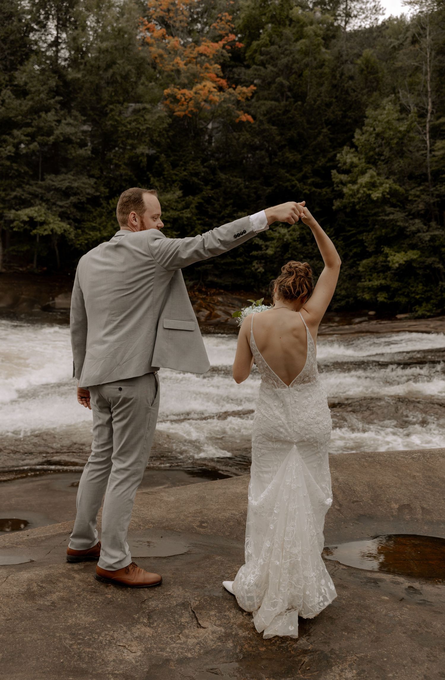 Elegant couple performs romantic dance on stone riverside with cascading waterfall in background.